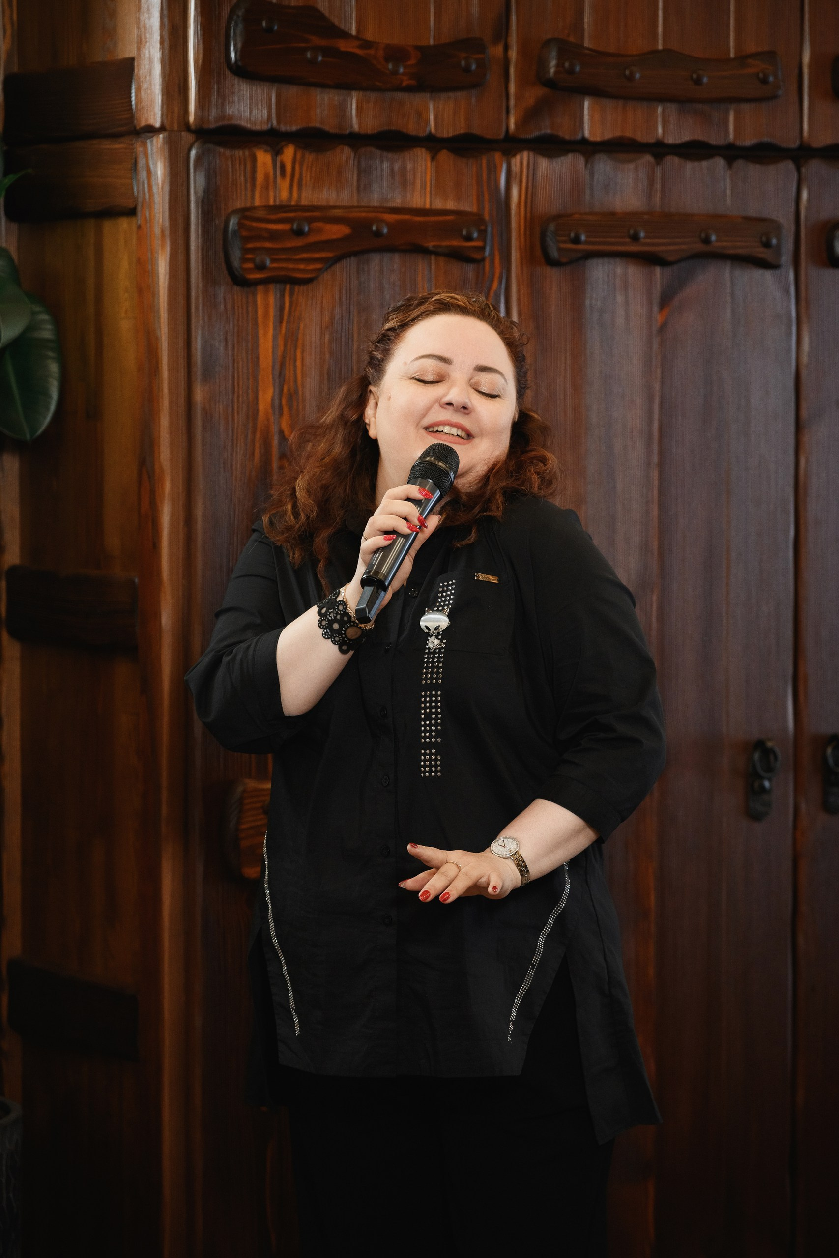 Женщина поёт с микрофоном на семейном празднике в уютном зале с деревянным интерьером, репортажная съёмка, Петропавловск-Камчатский.