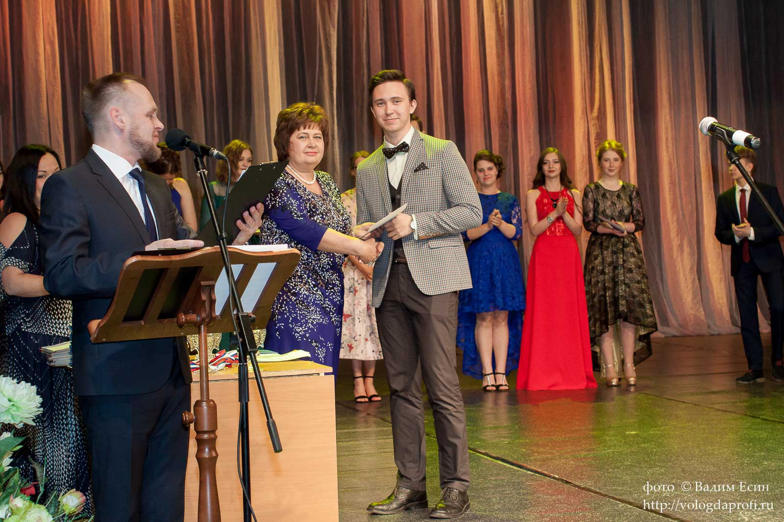 Торжественное вручение аттестата выпускнику 11 класса в сером пиджаке на сцене.