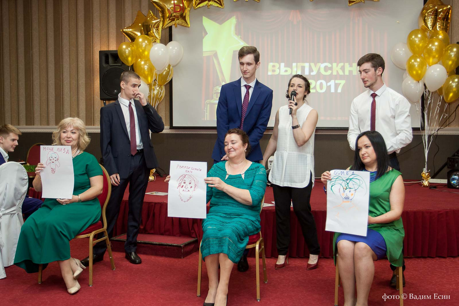 Три женщины в зеленых платьях держат в руках листы бумаги с личными портретами.