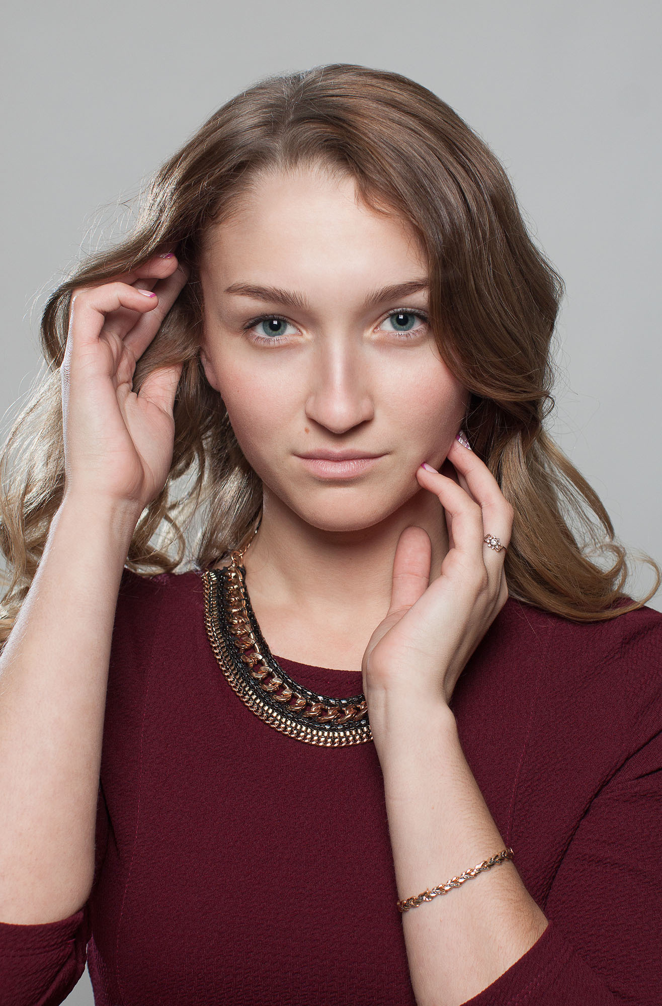 Погрудный портрет девушки с длинными волосами в бордовом платье на светло-сером фоне