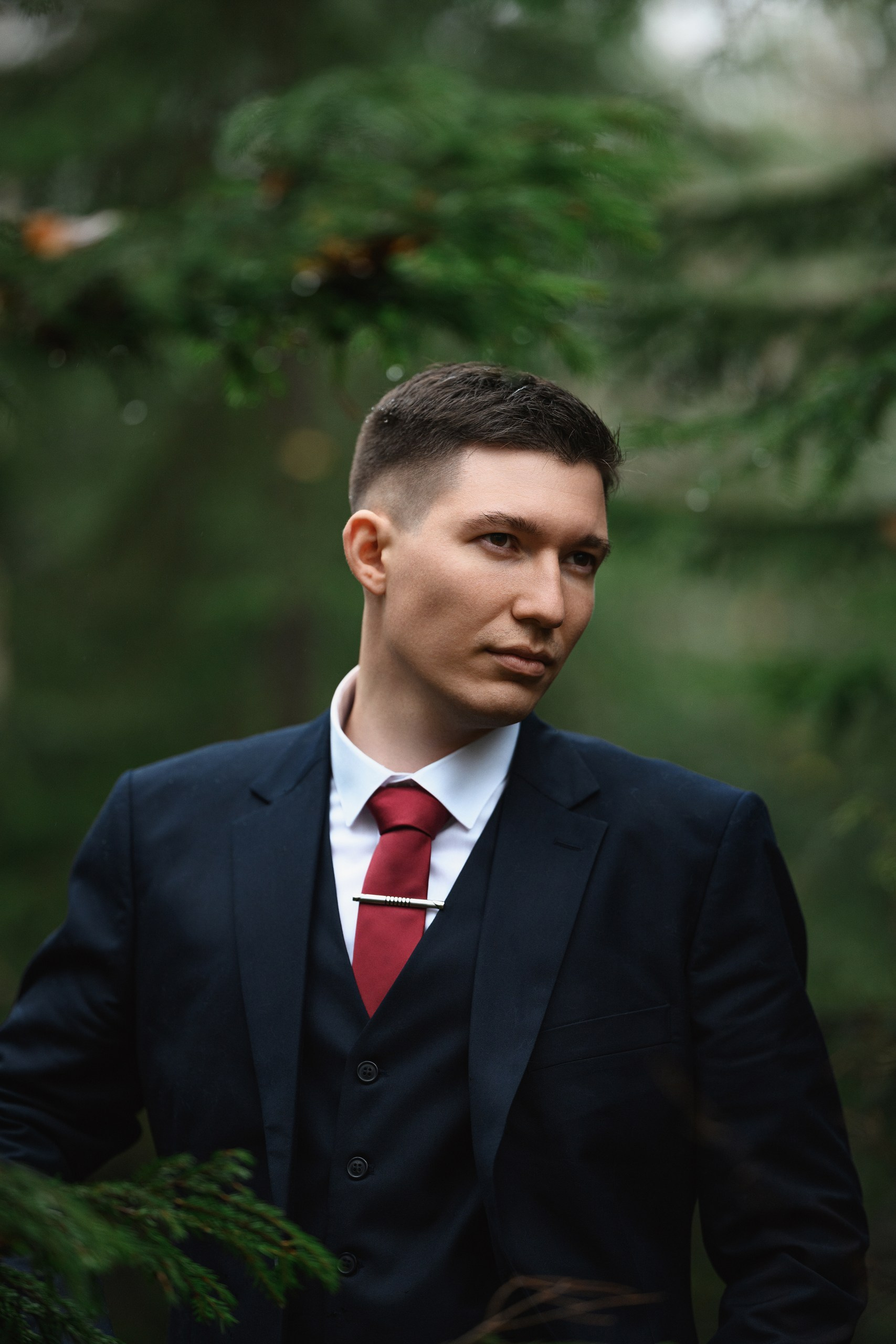 Индивидуальный портрет жениха в тёмном костюме на фоне зелёных деревьев