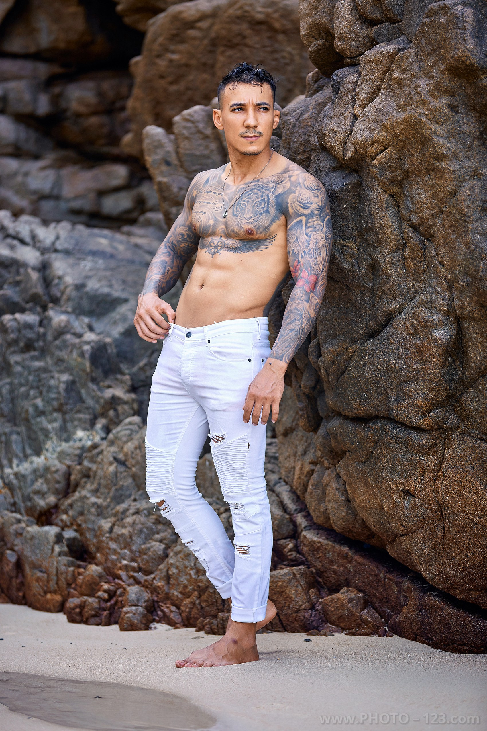 Full-length portrait of a shirtless muscular man standing by beach rocks captured by Nha Trang photographer