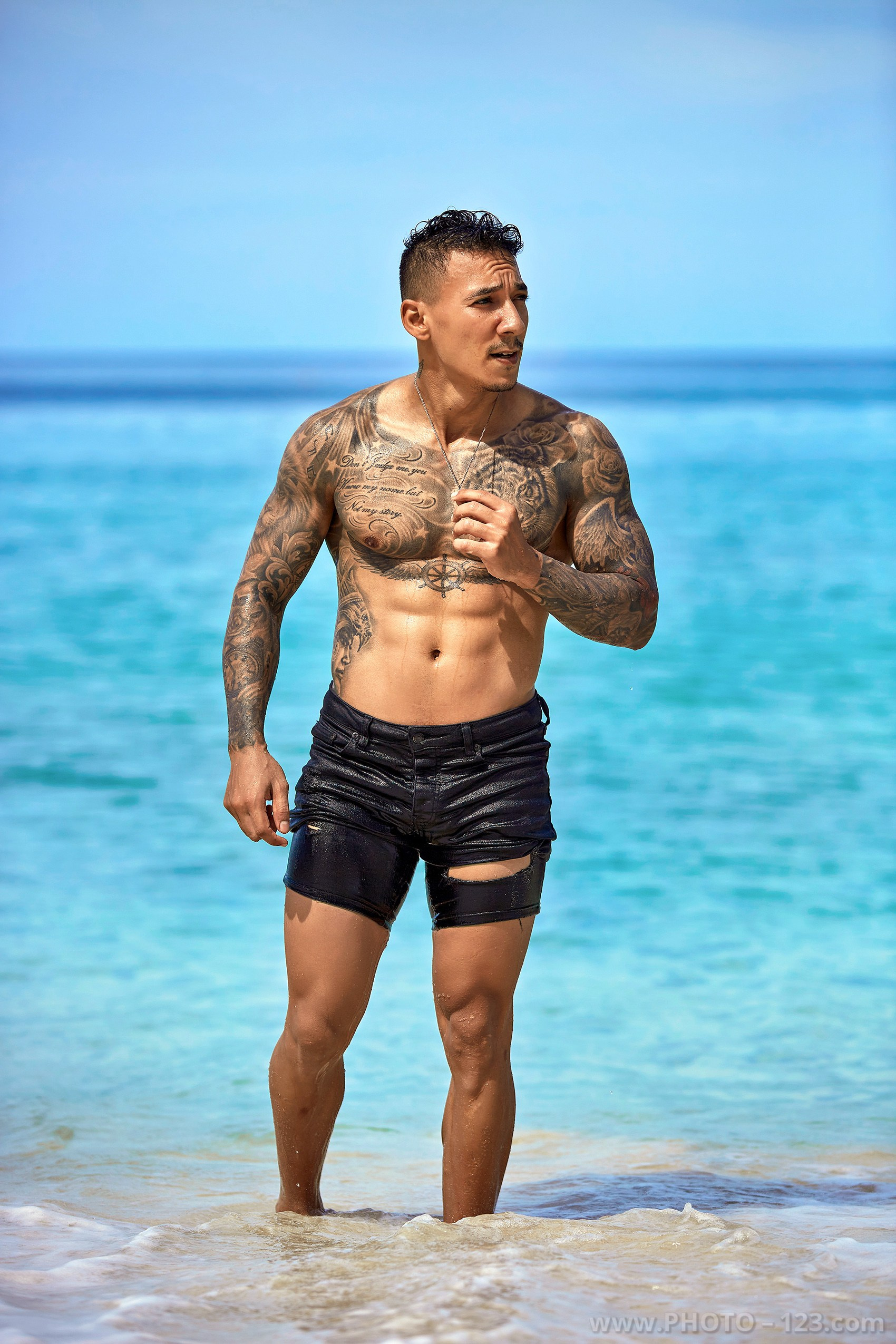 Shirtless fitness model standing in shallow sea water on a Nha Trang beach captured by local photographer