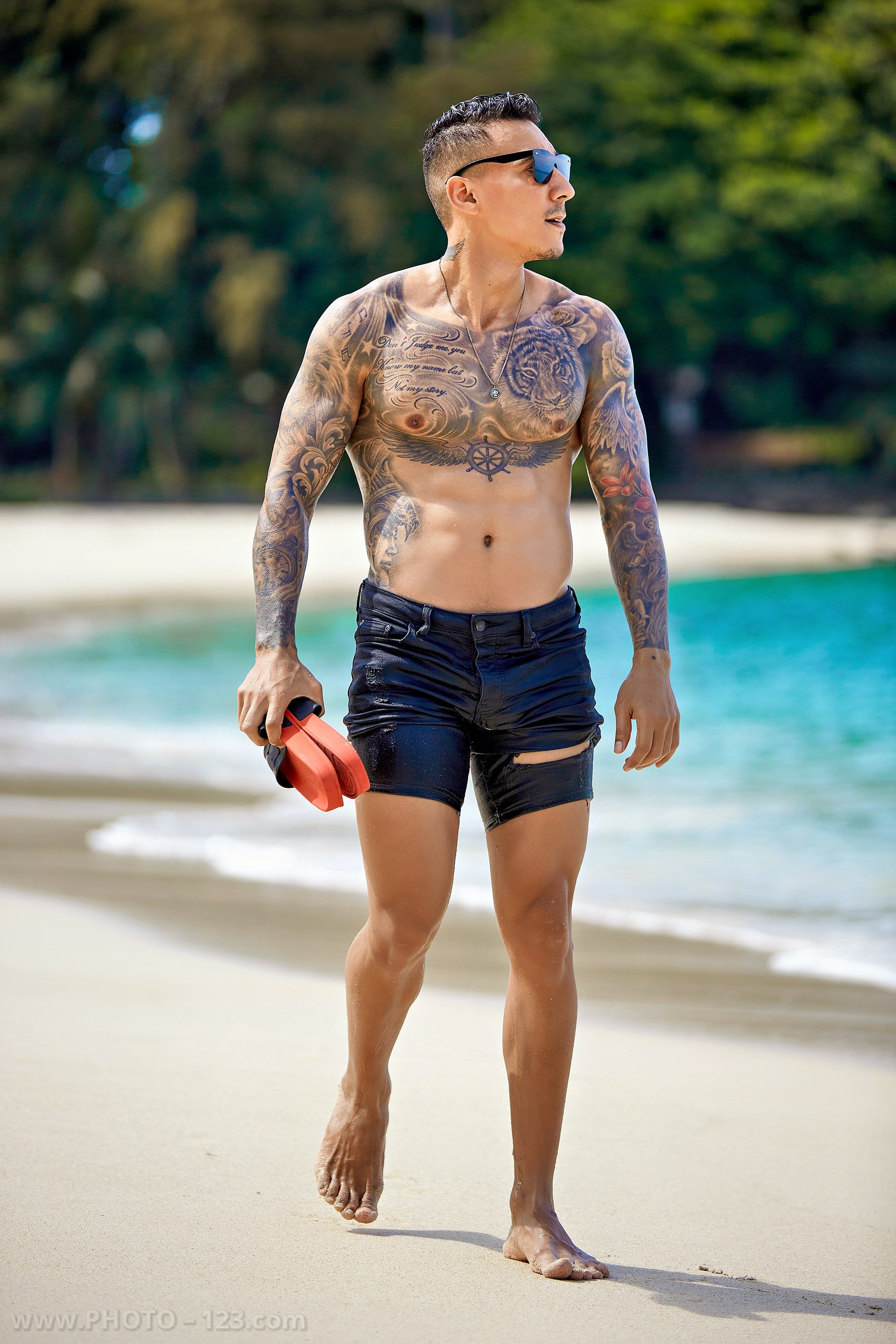 Muscular tattooed man holding swim fins walking on a sandy beach in Nha Trang