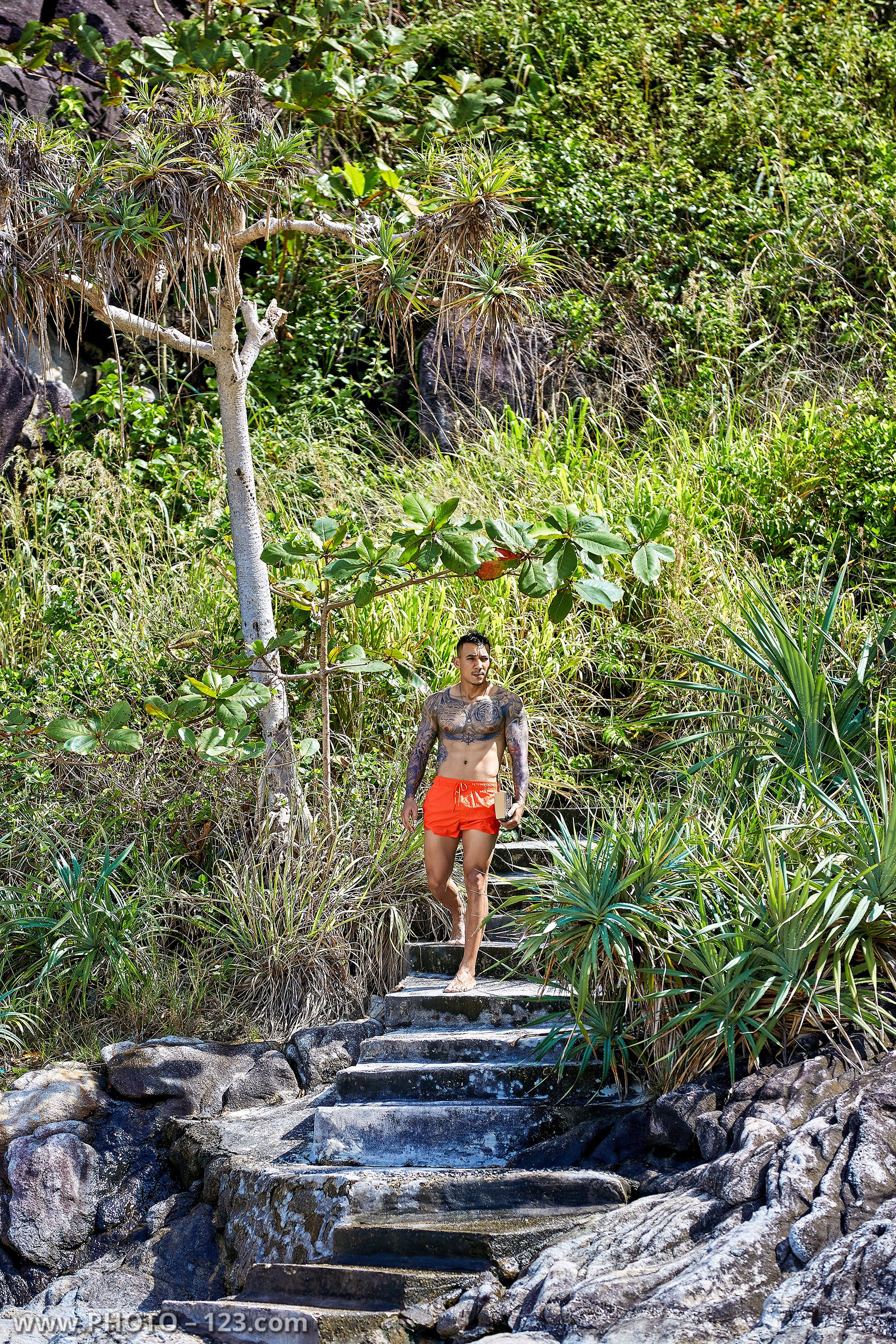 Muscular man walking down stone steps surrounded by tropical greenery on a Nha Trang beach