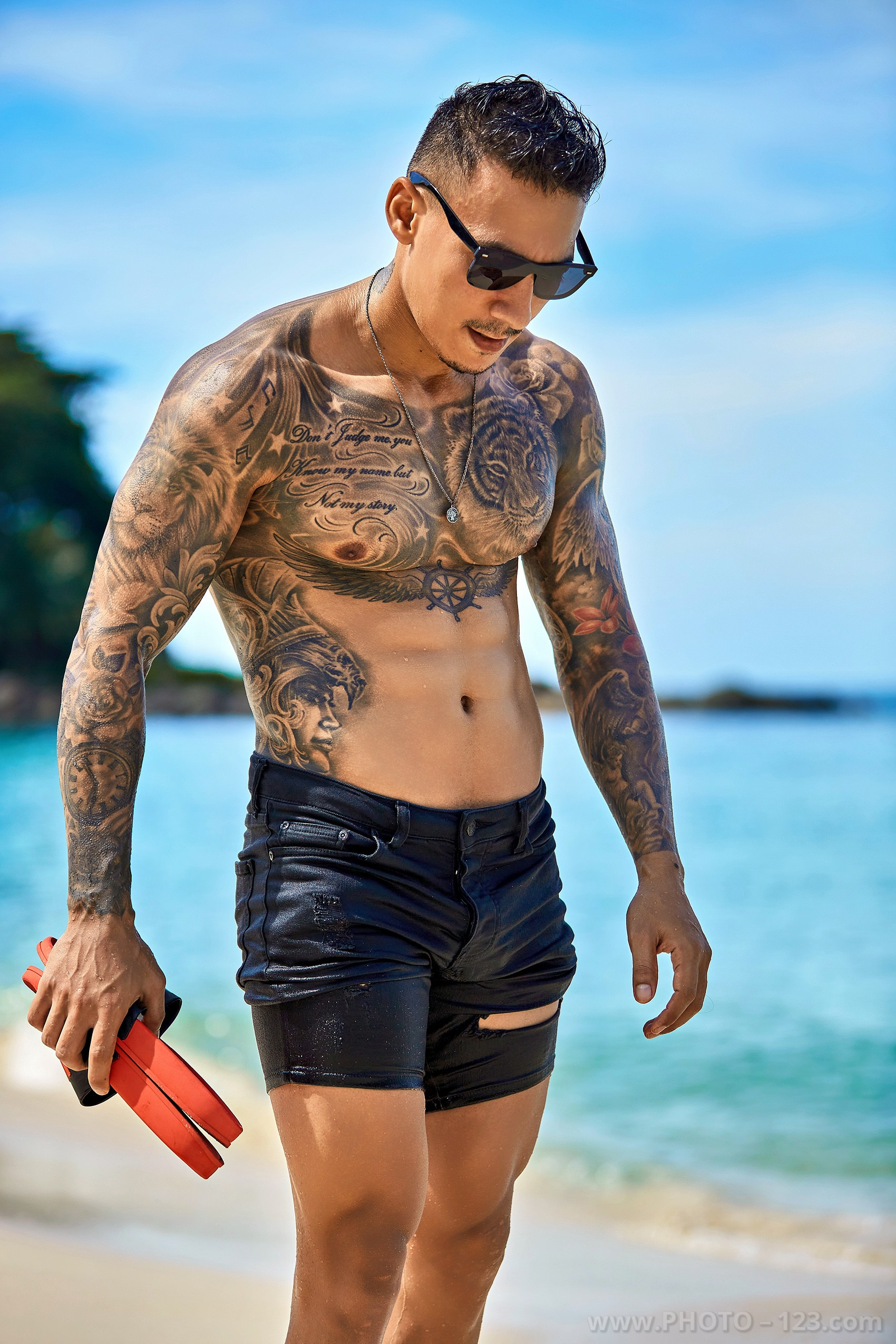 Shirtless man in sunglasses holding flippers on a tropical beach captured by Nha Trang photographer