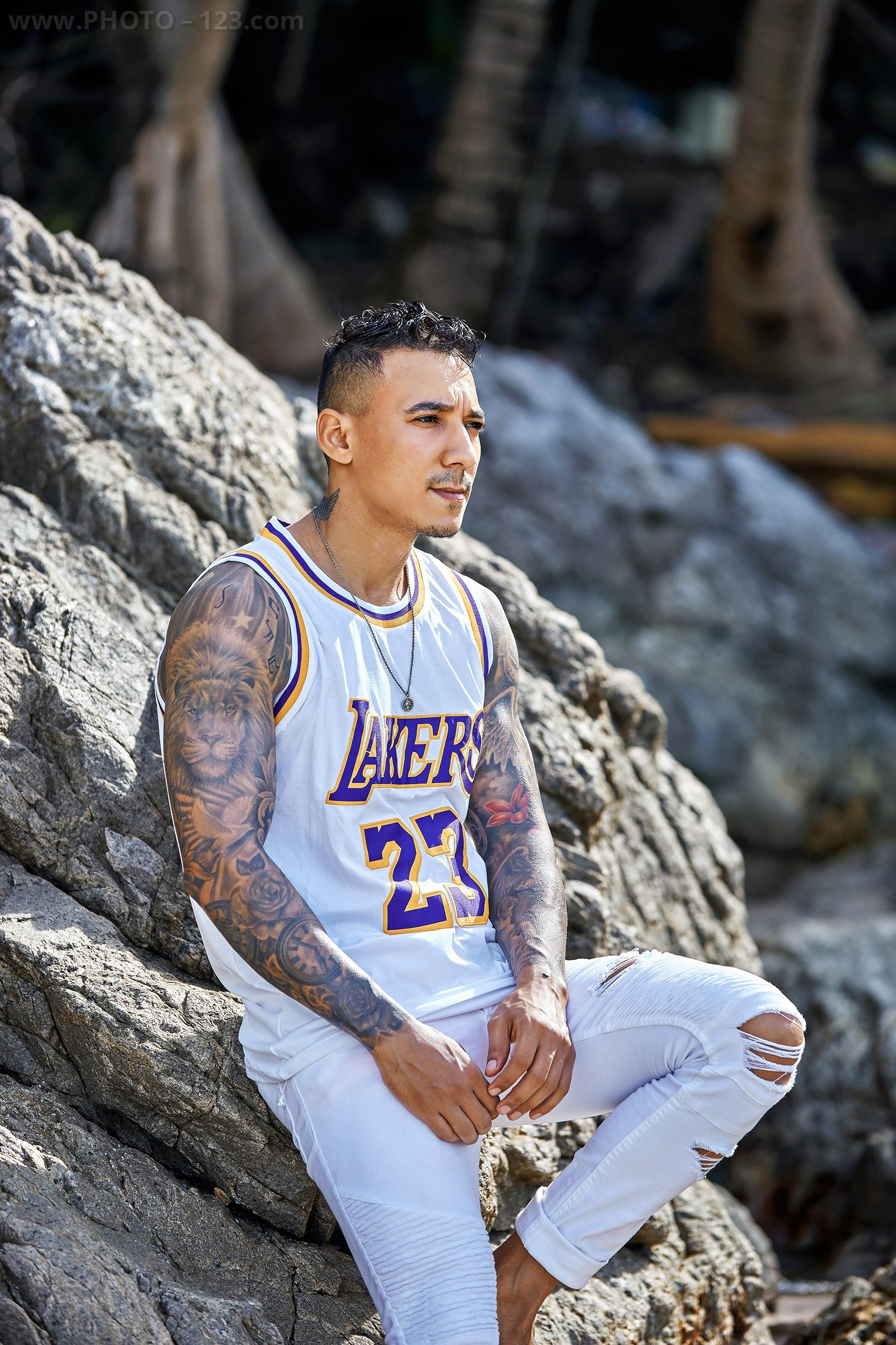 Muscular man posing on rocky seashore in white athletic wear captured by Nha Trang photographer
