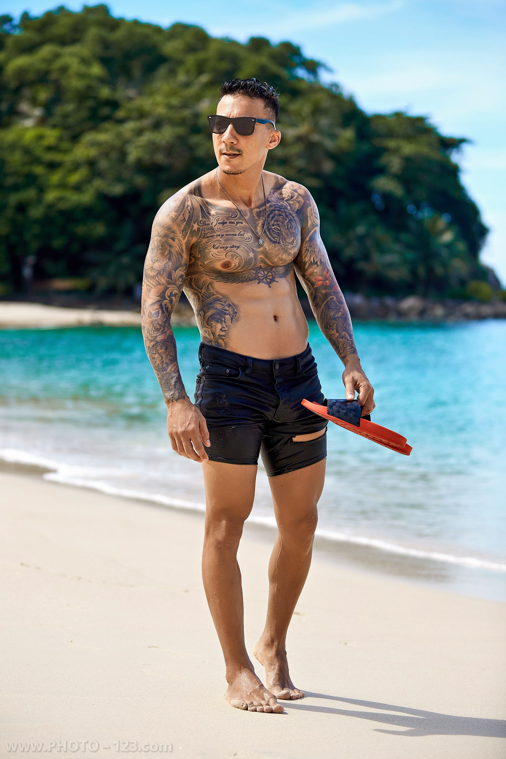 Athletic male model walking along the shoreline with red flippers during a Nha Trang photoshoot