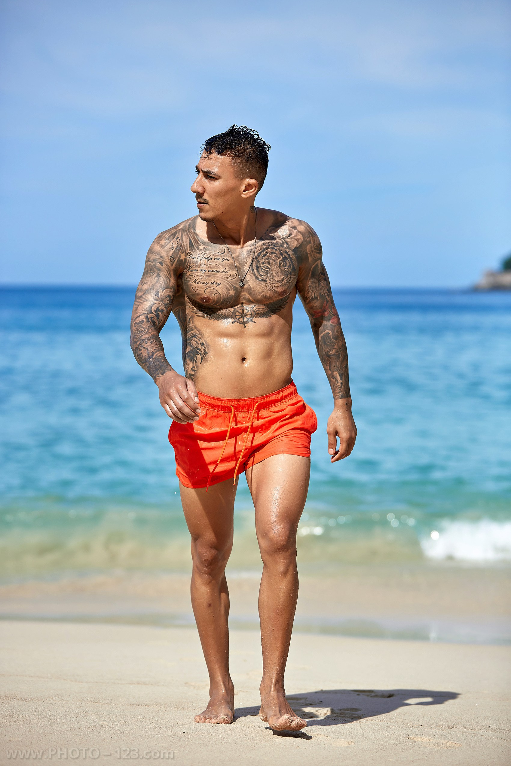 Athletic man walking along the sandy shoreline during a male beach photoshoot in Nha Trang