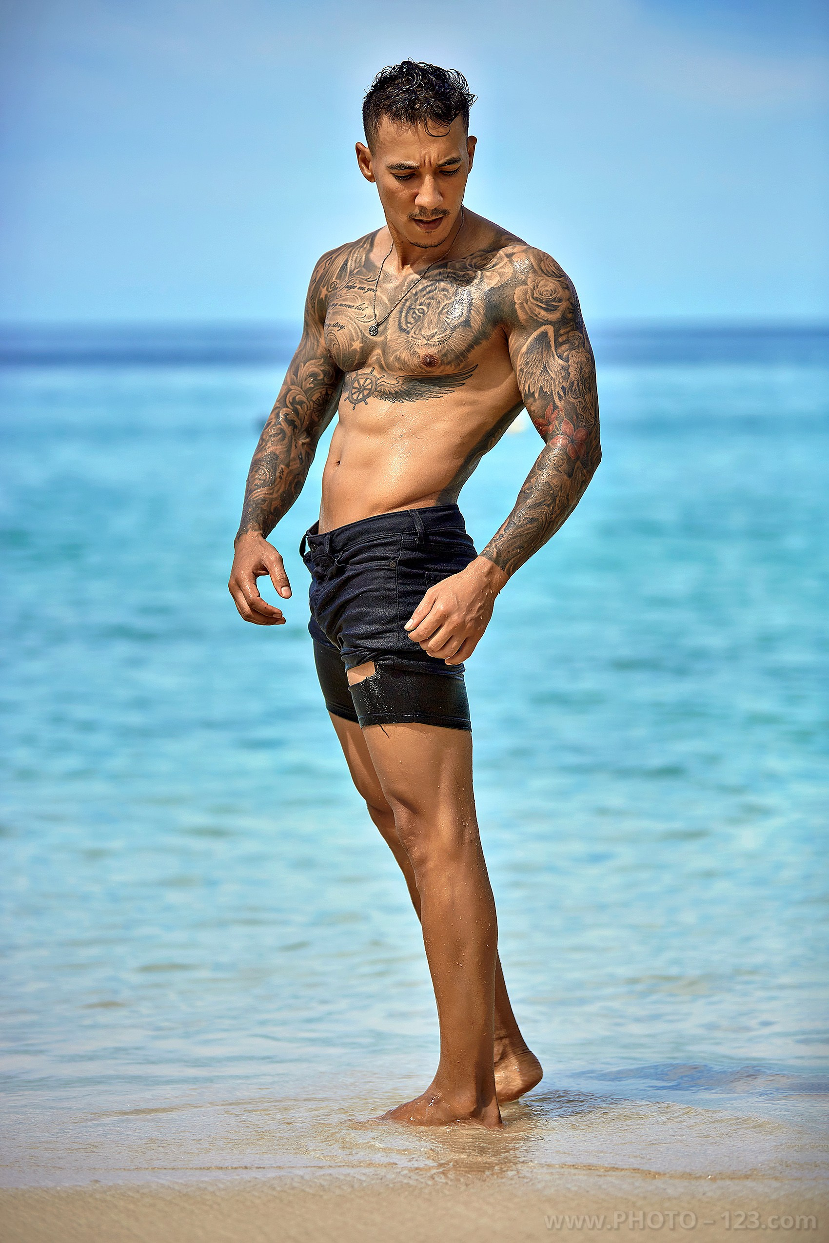Tattooed fitness male model posing on the shoreline of a Nha Trang beach by local photographer