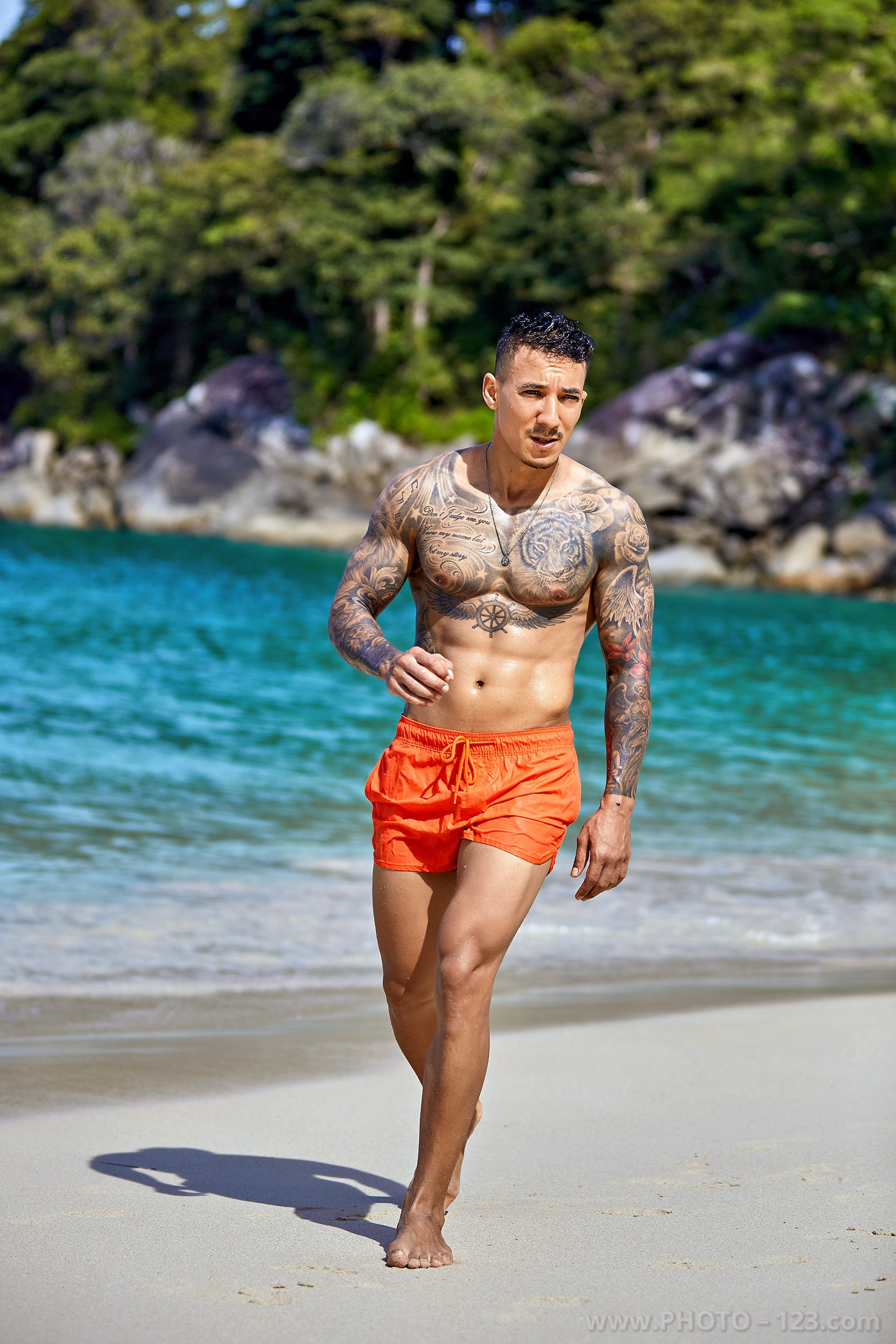 Shirtless tattooed man walking on a white sand beach in Nha Trang captured by local photographer