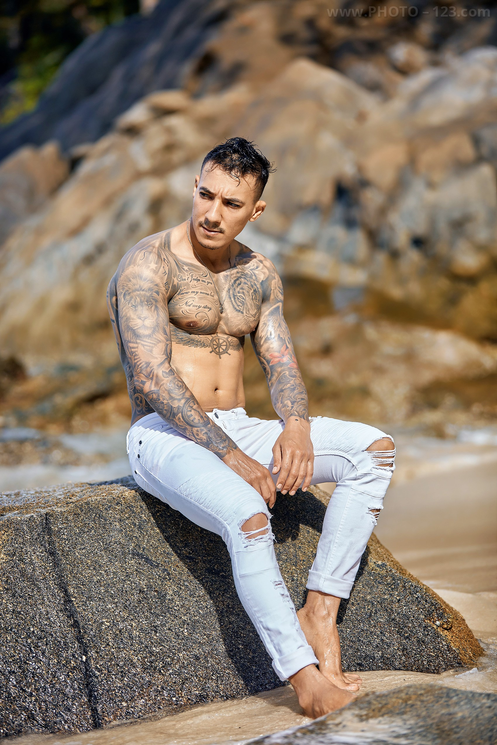 Athletic male model with tattoos posing on coastal rocks in Nha Trang Vietnam
