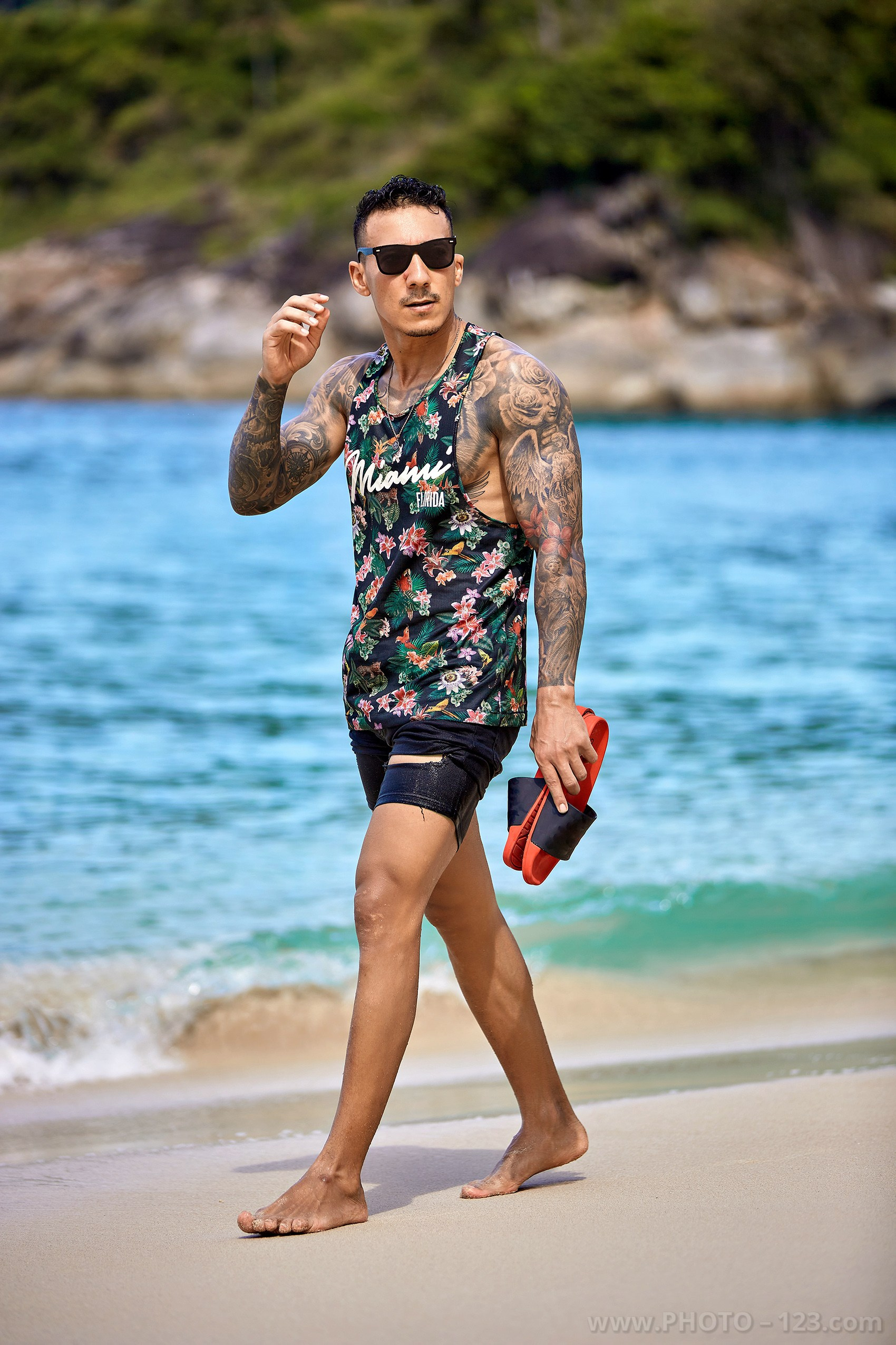 Muscular tattooed man in floral tank top carrying sandals on a beach in Nha Trang captured by local photographer