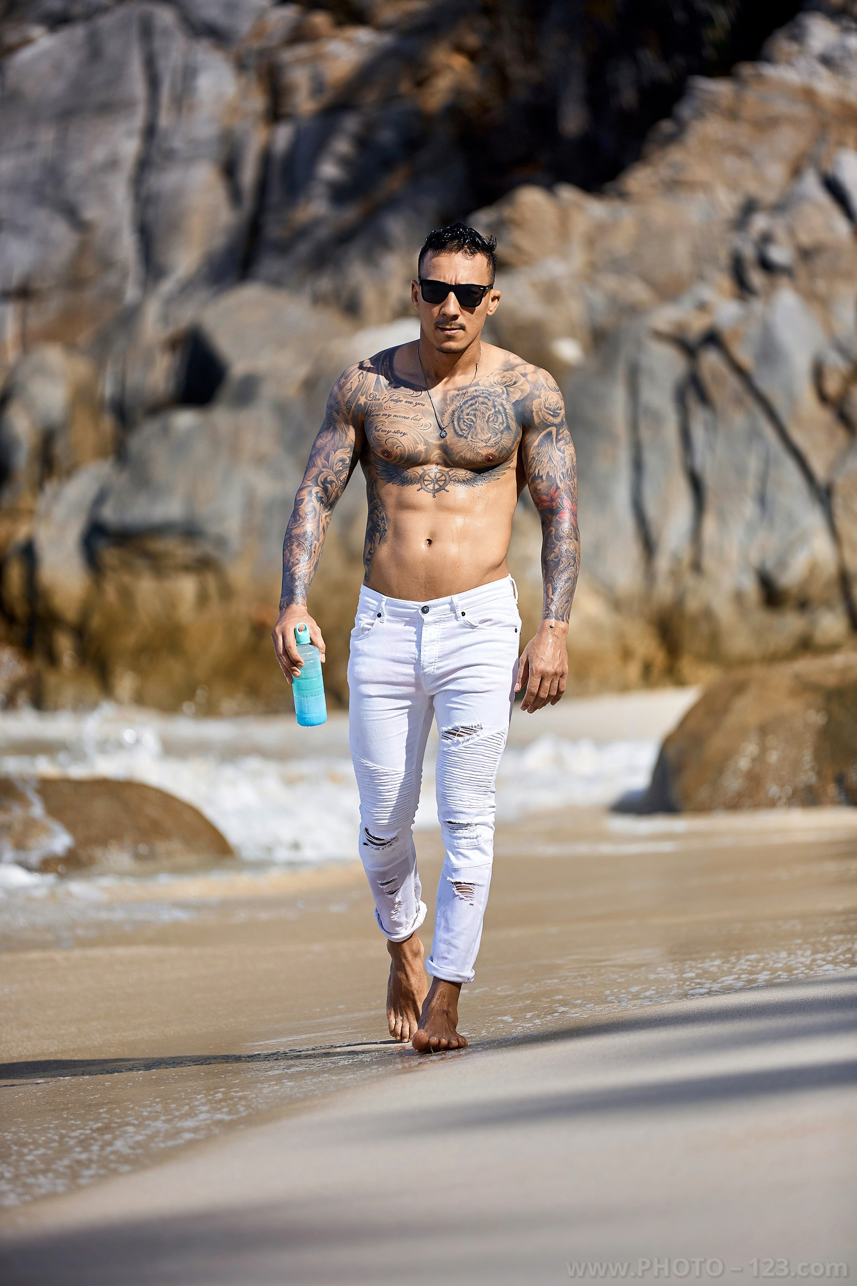 Muscular man in white jeans walking on the sandy shore during a beach photoshoot in Nha Trang
