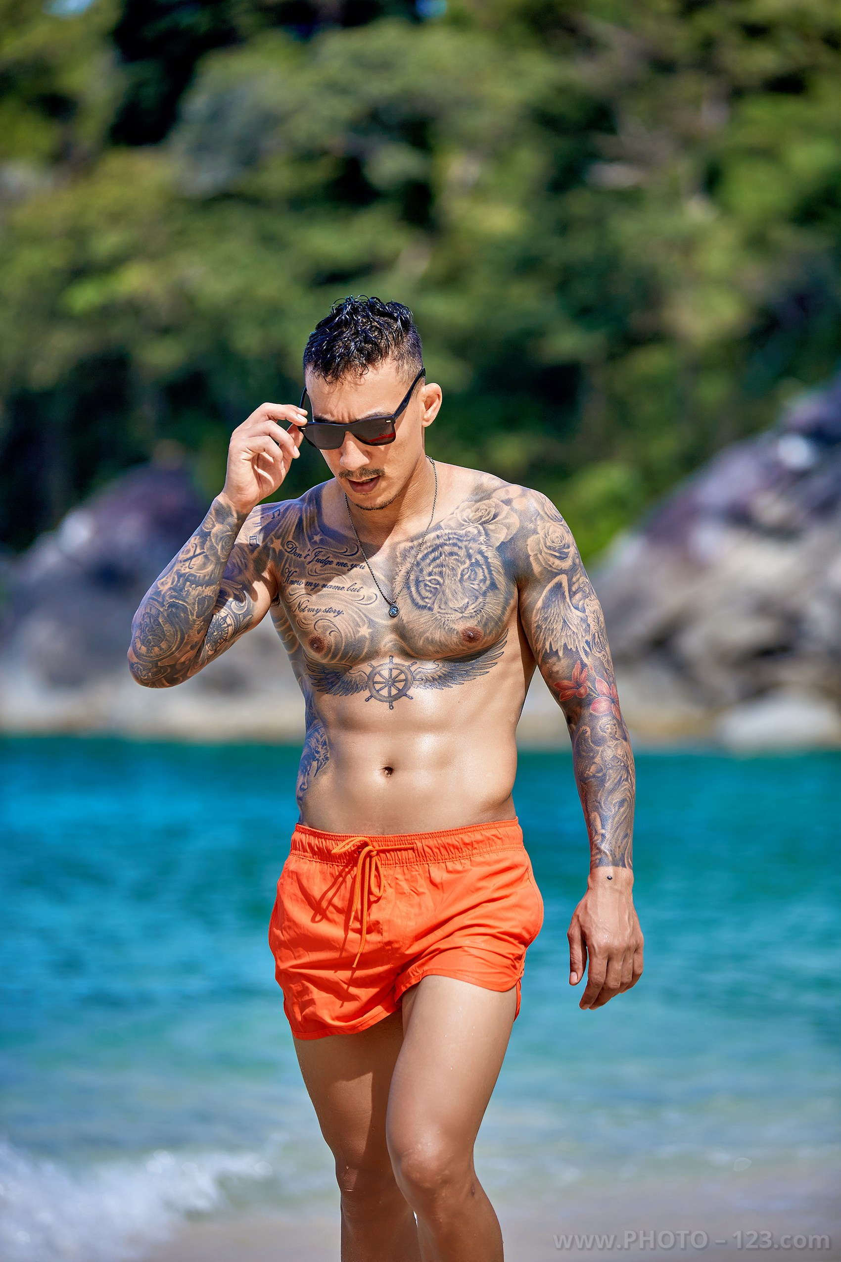 Tattooed male model adjusting sunglasses while walking out of the sea in Nha Trang