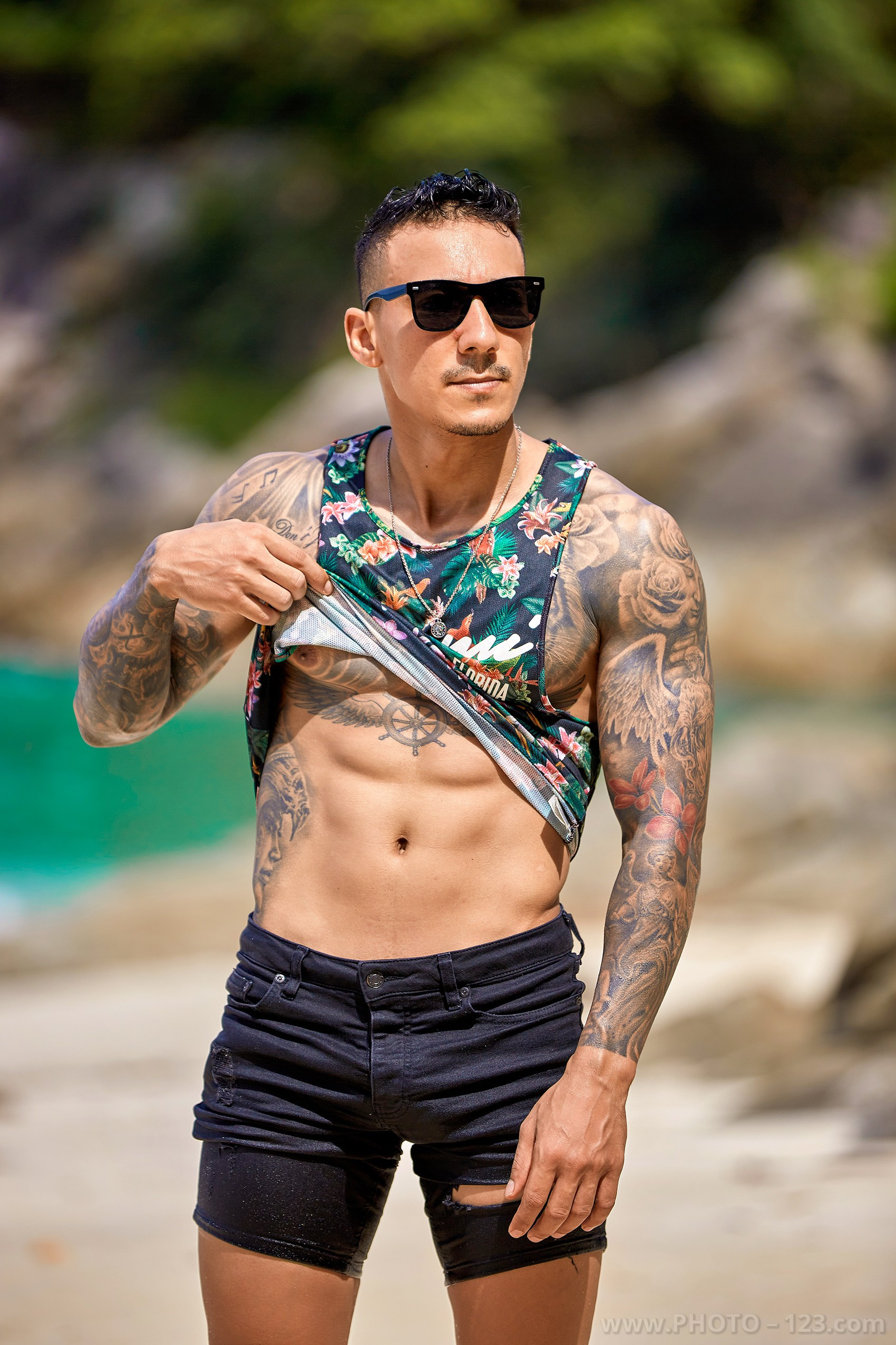 Athletic male model lifting tank top to show abs during a beach photoshoot in Nha Trang