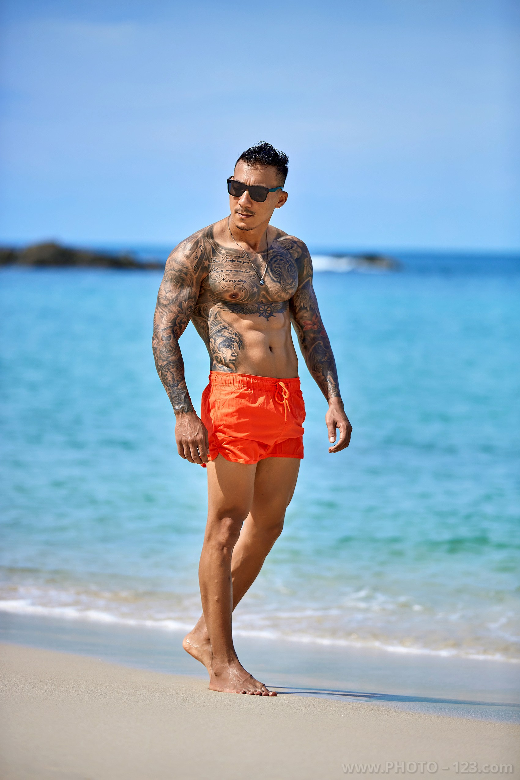 Muscular fitness model in sunglasses posing by the turquoise sea in Nha Trang by professional photographer