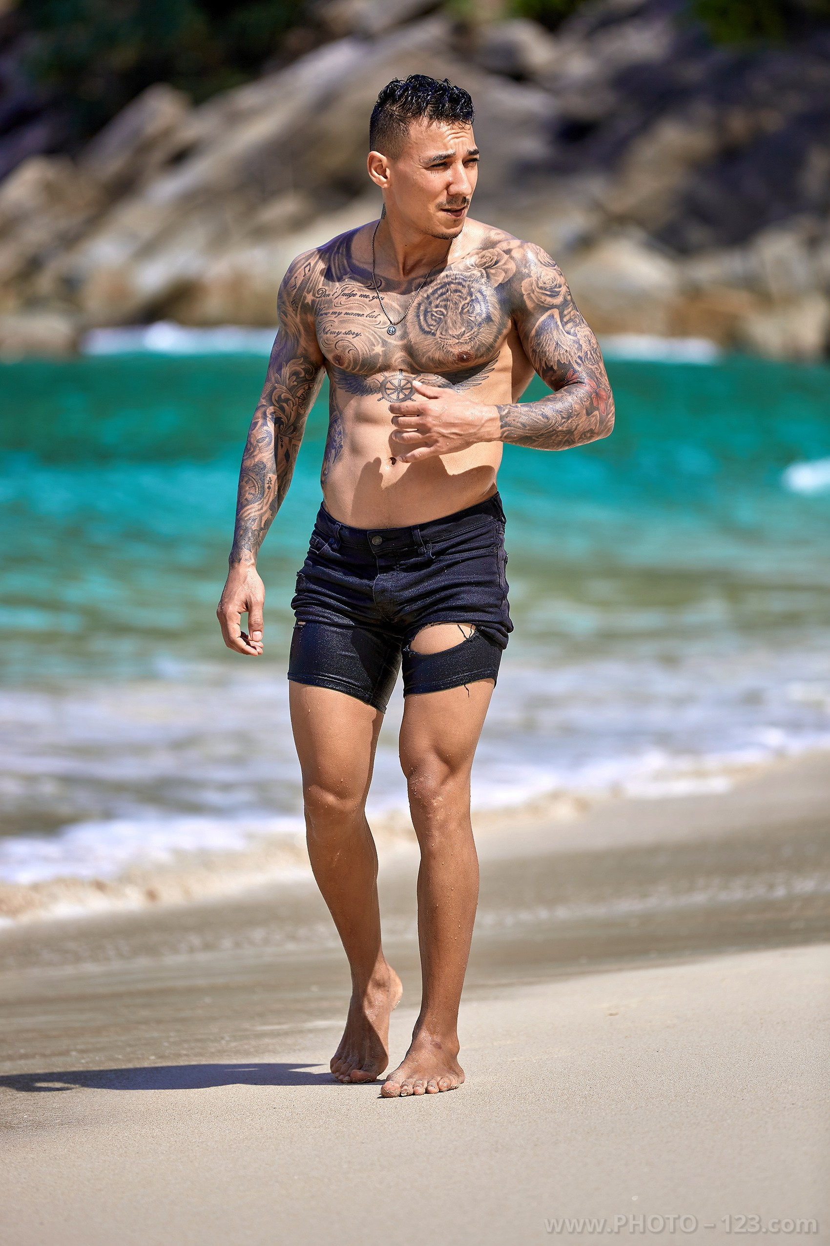 Full-length portrait of an athletic man in black shorts walking on the beach in Nha Trang