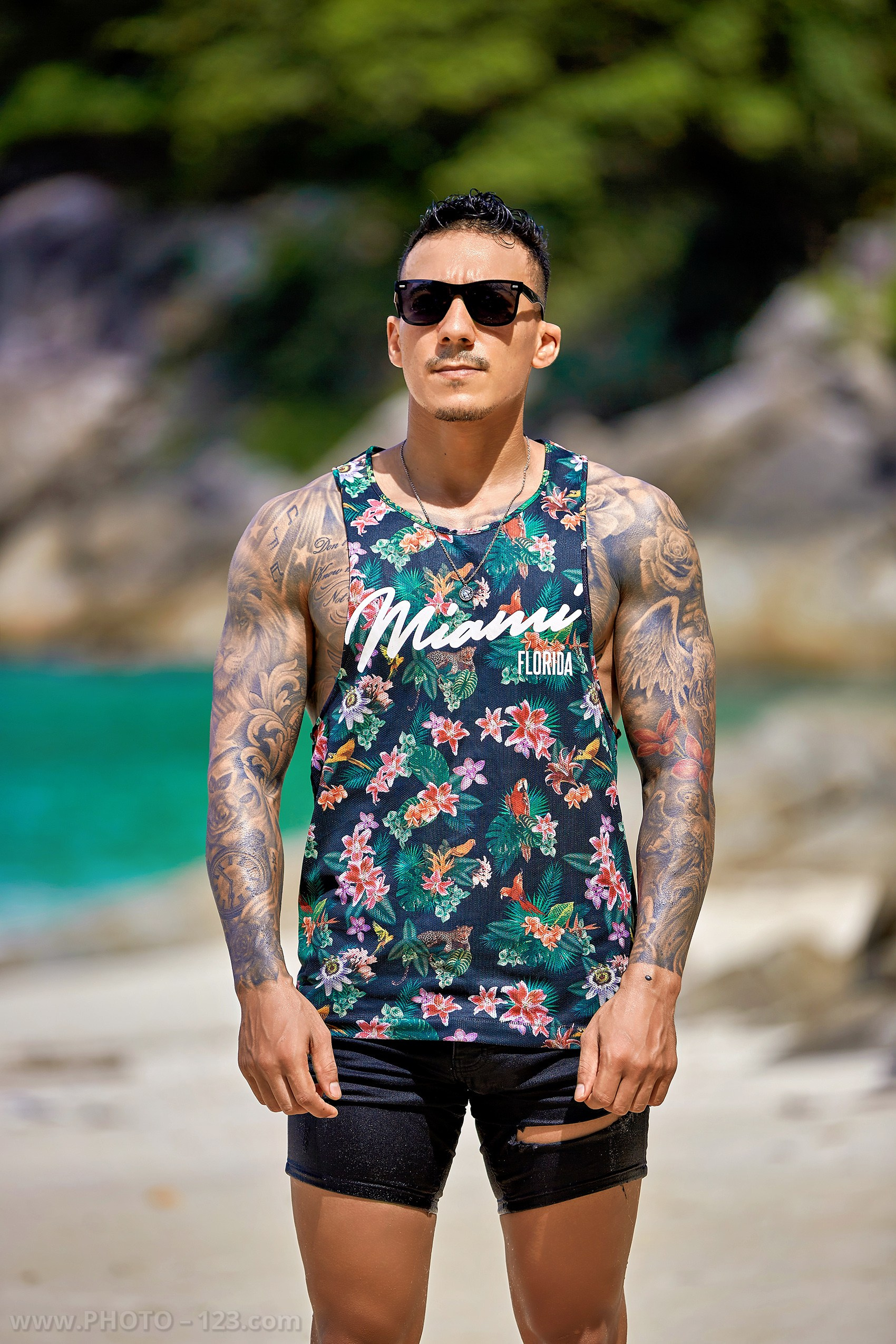 Tattooed man in sunglasses and floral tank top posing on a beach in Nha Trang Vietnam