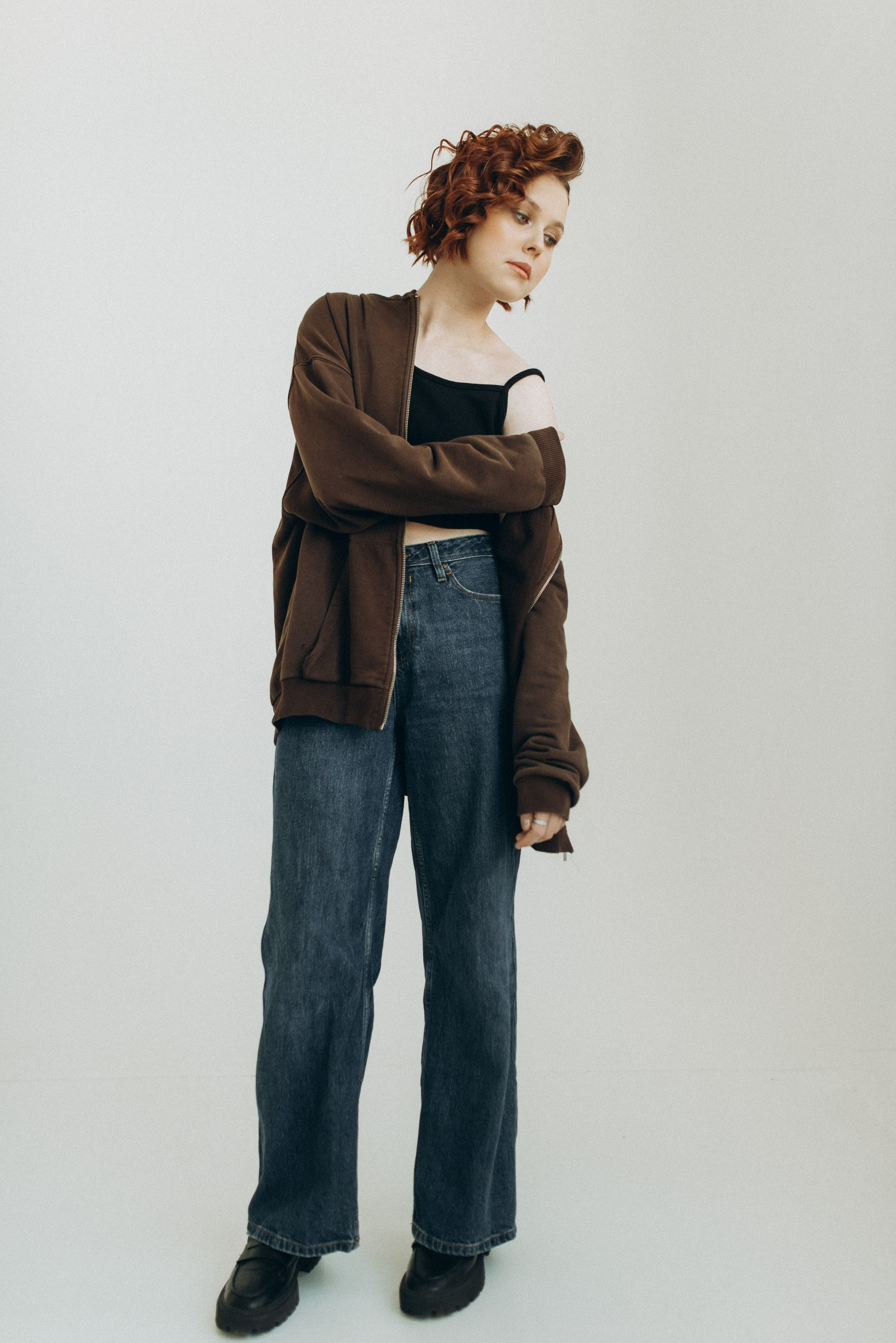 Девушка-подросток в полный рост в коричневой худи и широких джинсах. Стильная фотосессия в светлой студии Новосибирска