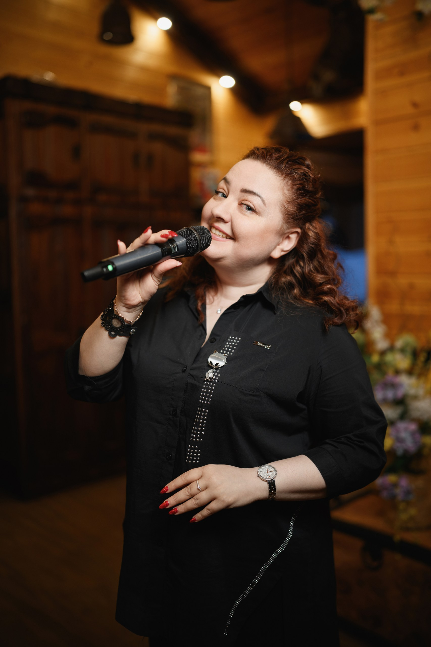 Женщина поёт с микрофоном на семейном празднике в уютном зале с деревянным интерьером, репортажная съёмка, Петропавловск-Камчатский.