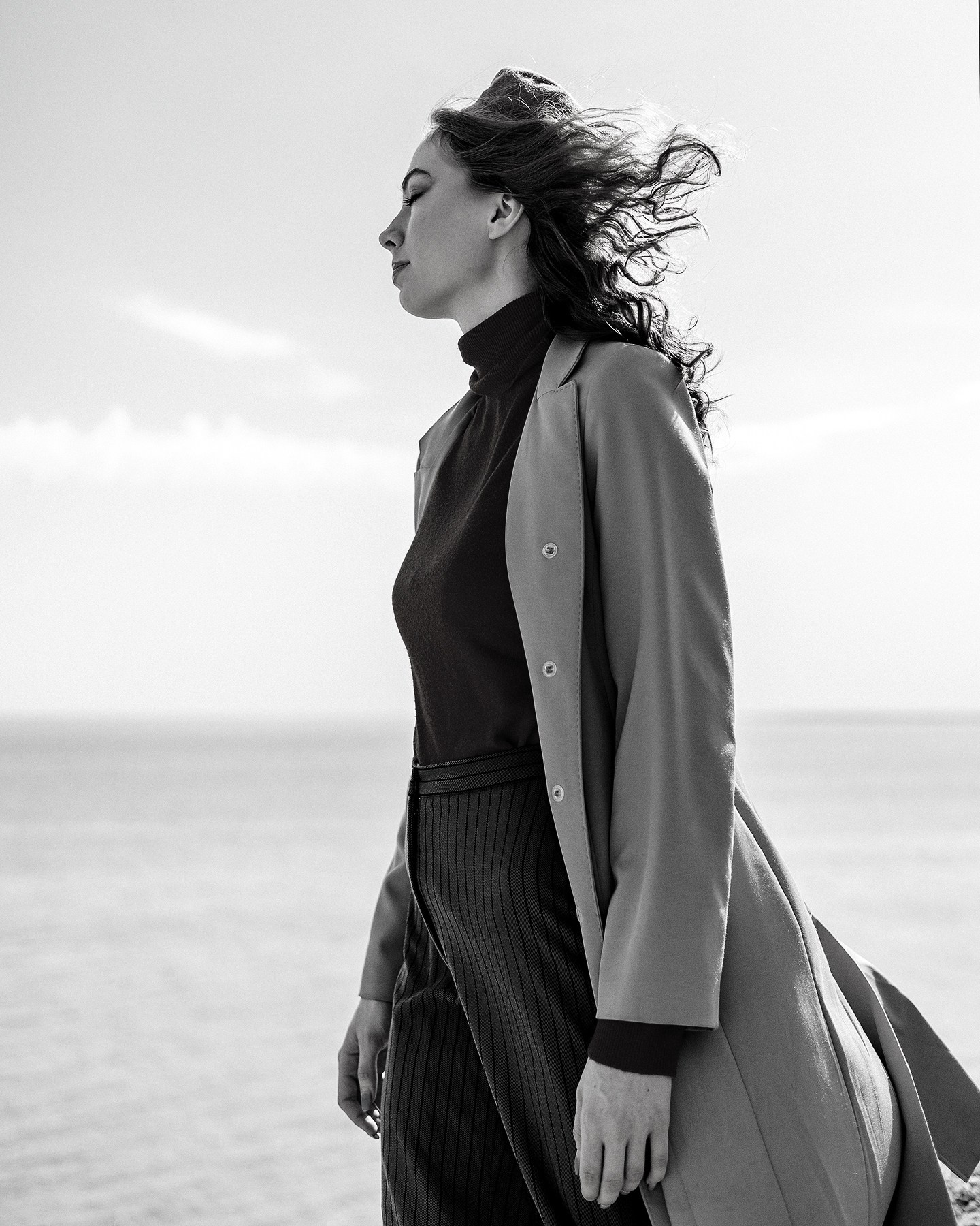 молодая девушка в пальто и берете позирует на фоне воды