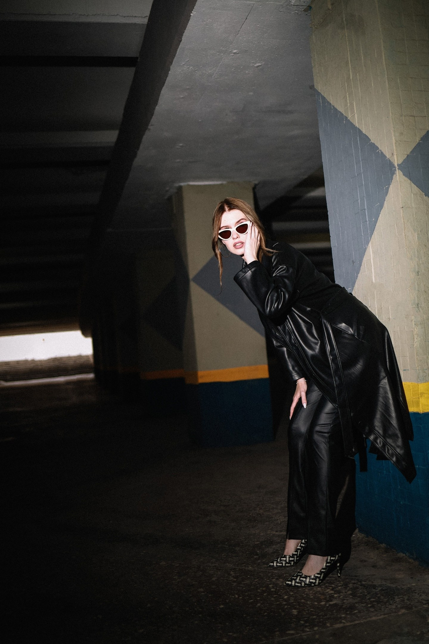 Девушка в "total black" - очки, черный плащ в помещении, похожем на ангар, недалеко от метро