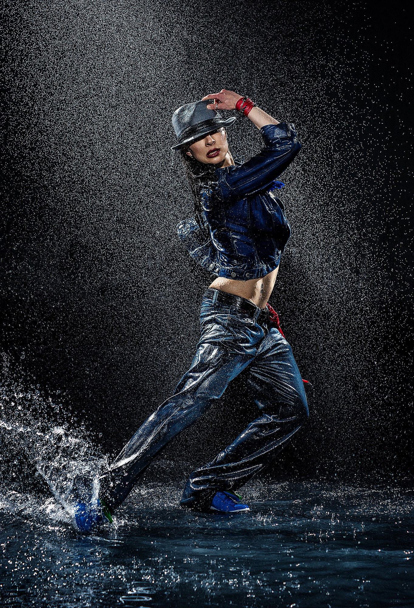 Стрит-дансер в прыжке под мощным дождевым потоком, яркие брызги подчёркивают силу движения. Динамичная уличная танцевальная съёмка в Москве и Истринском районе.