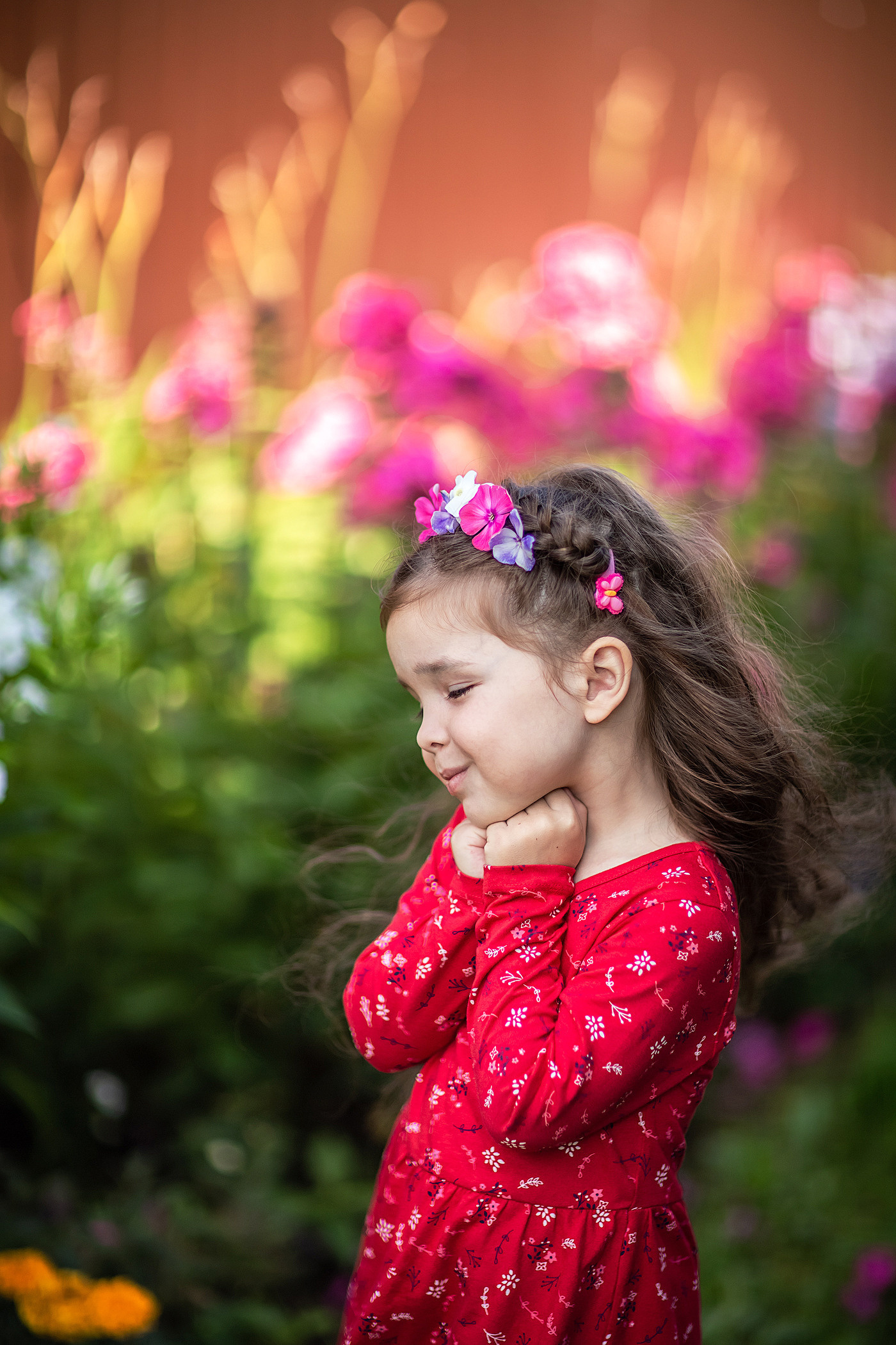 девочка в ободке из цветов и красном плате умиляется цветами в саду