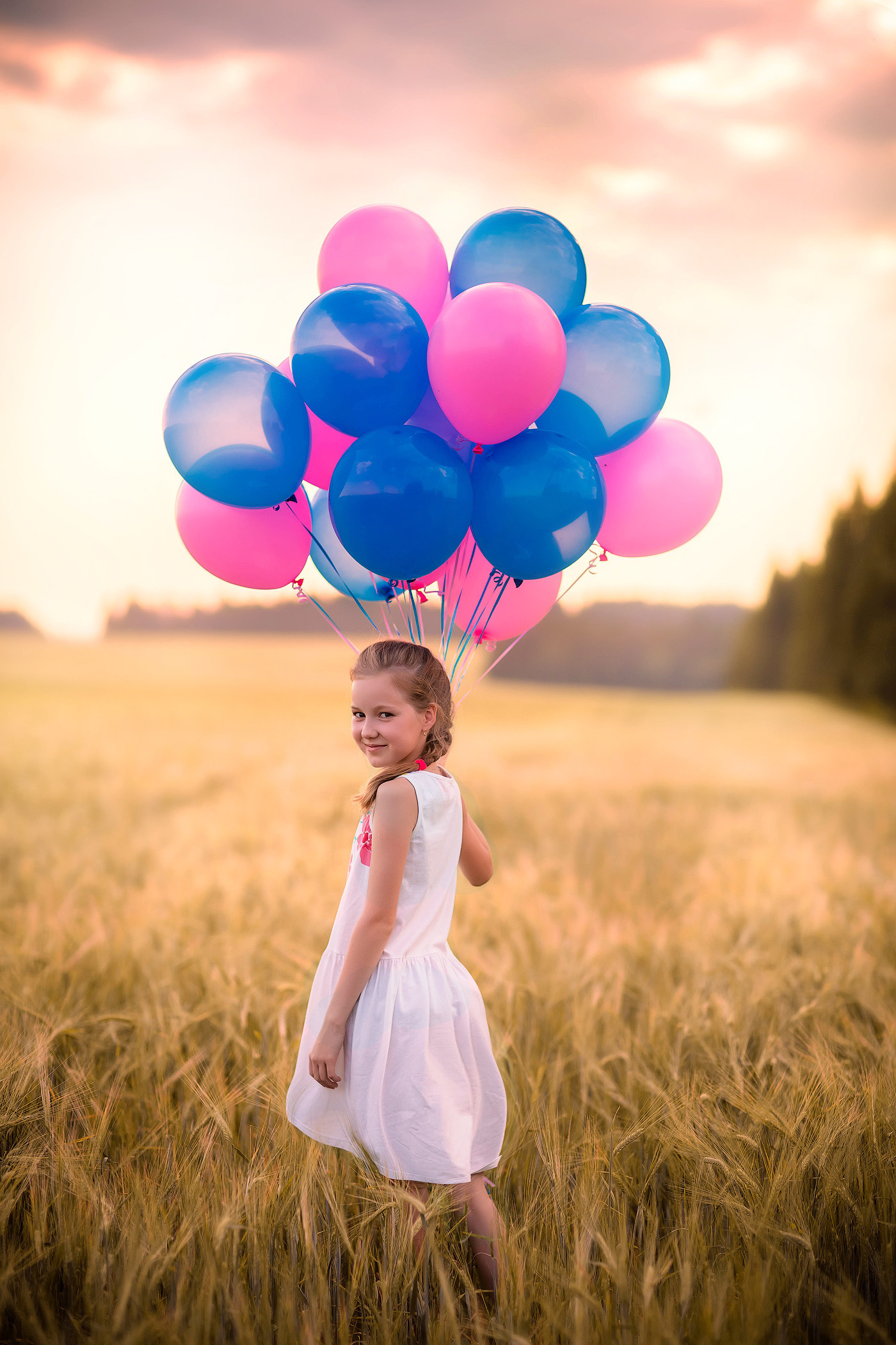 девочка в белом платье с охапкой разноцветных шаров бежит по пшеничному полю на закате