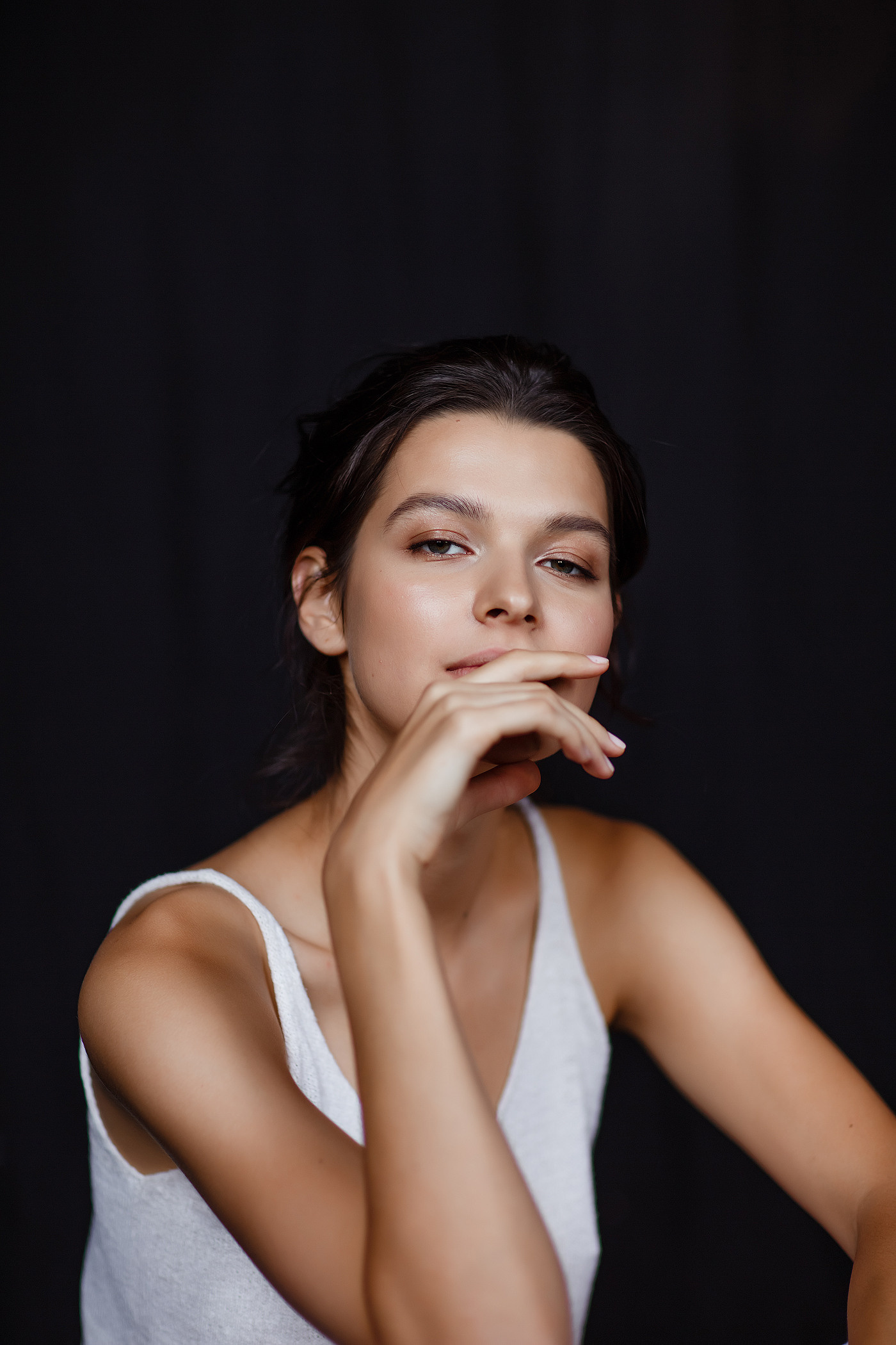 портрет красивой девушки брюнетки с чёрными волосами в белом топе на черном фоне