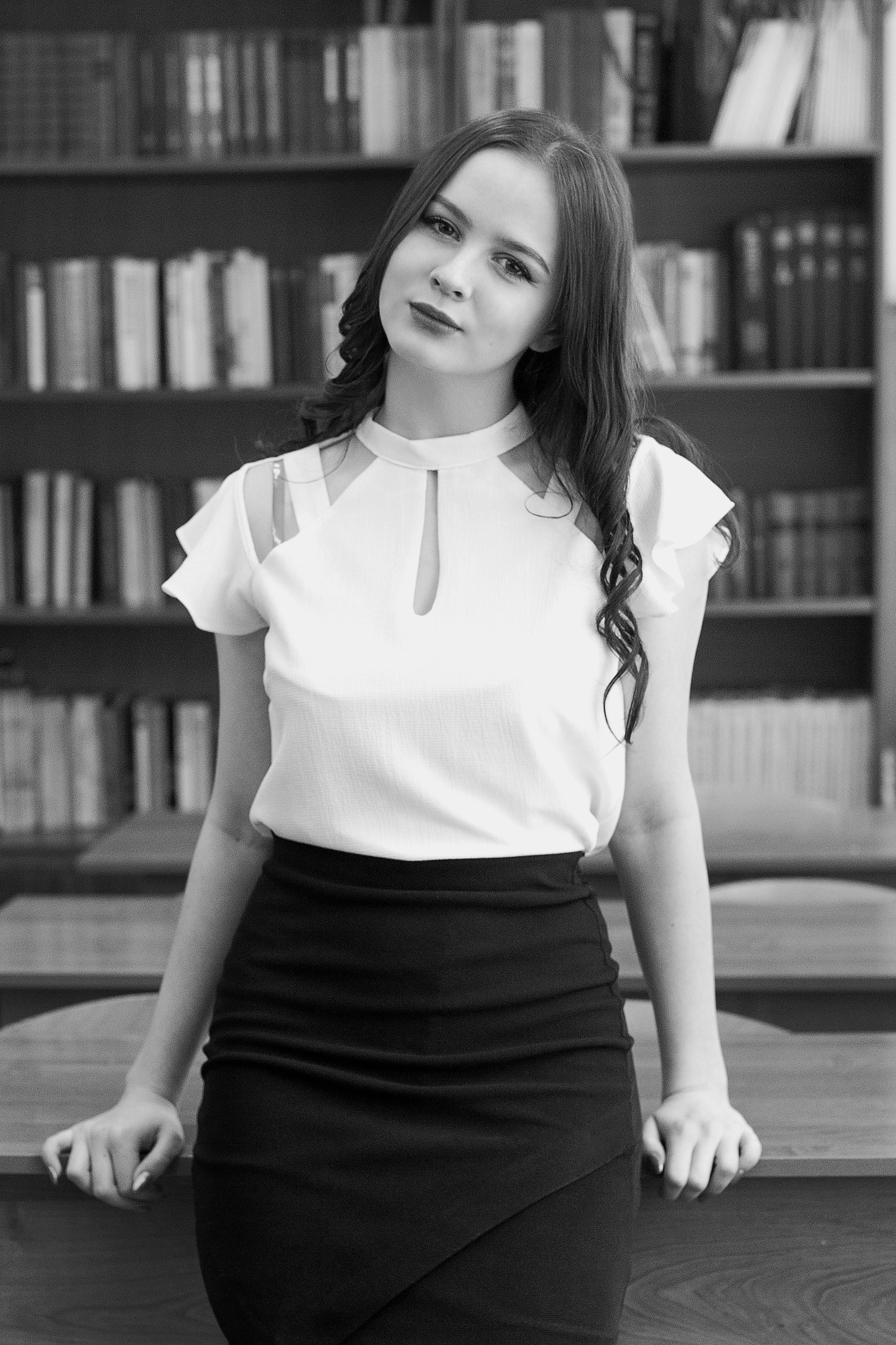 Школьный портрет выпускницы у книжного шкафа для выпускного альбома 9–11 класса