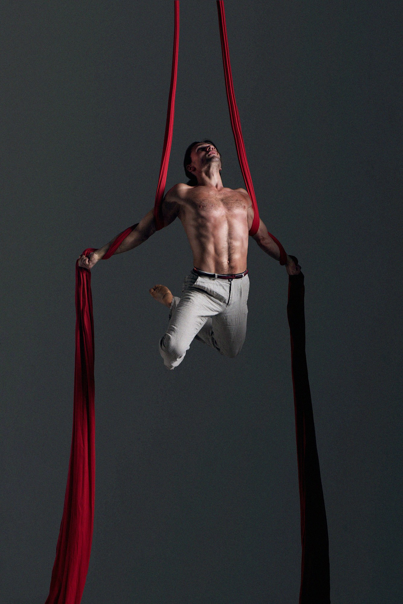 Акробатка выполняет классическую вертикальную стойку на красных полотнах, вытягивая корпус и руки. Сдержанный фон подчёркивает чистоту линии. Профессиональная съёмка воздушной гимнастики, Москва и Истринский район.