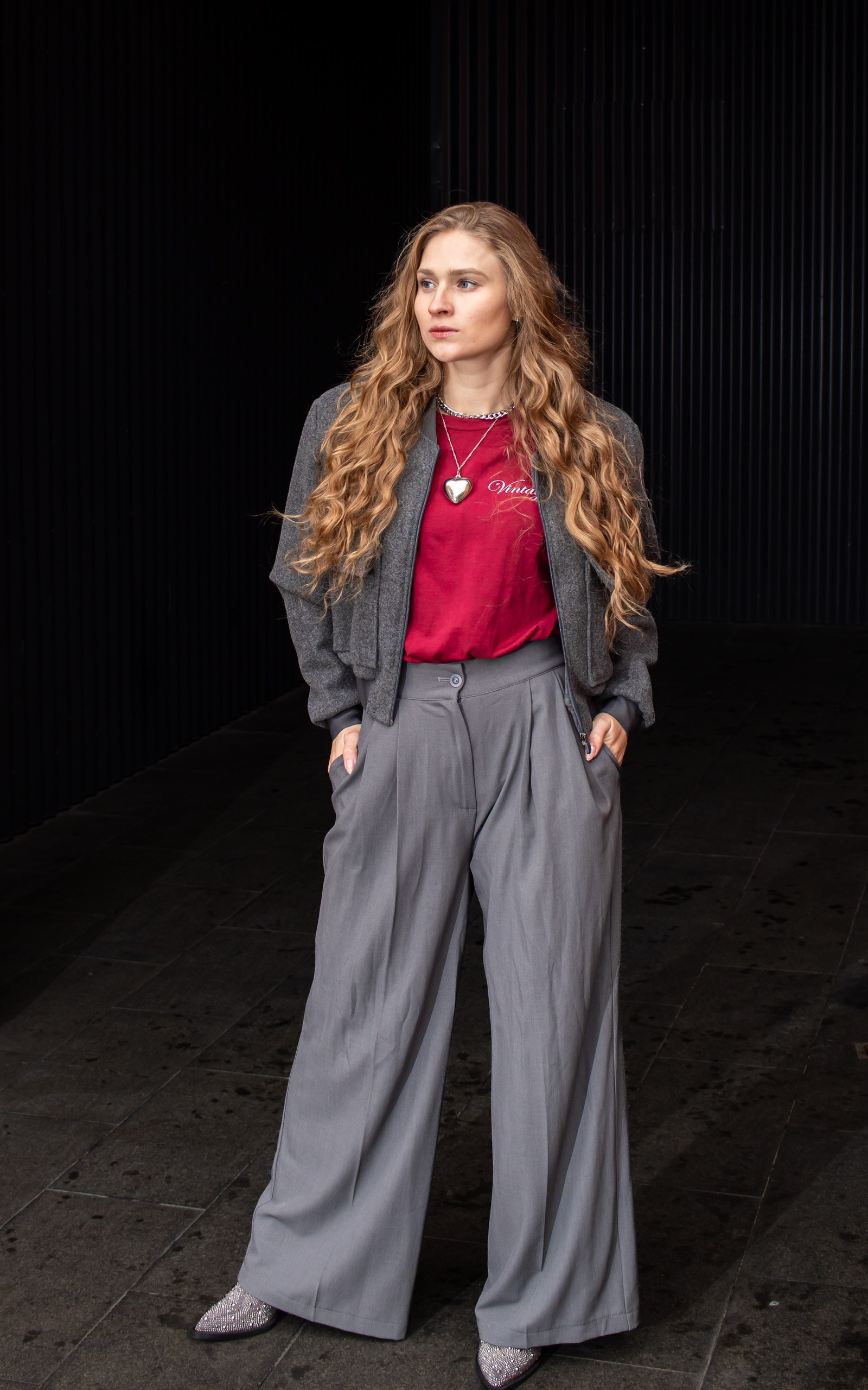 Модель позирует у чёрной стены, длинные волнистые волосы, стильный осенний образ