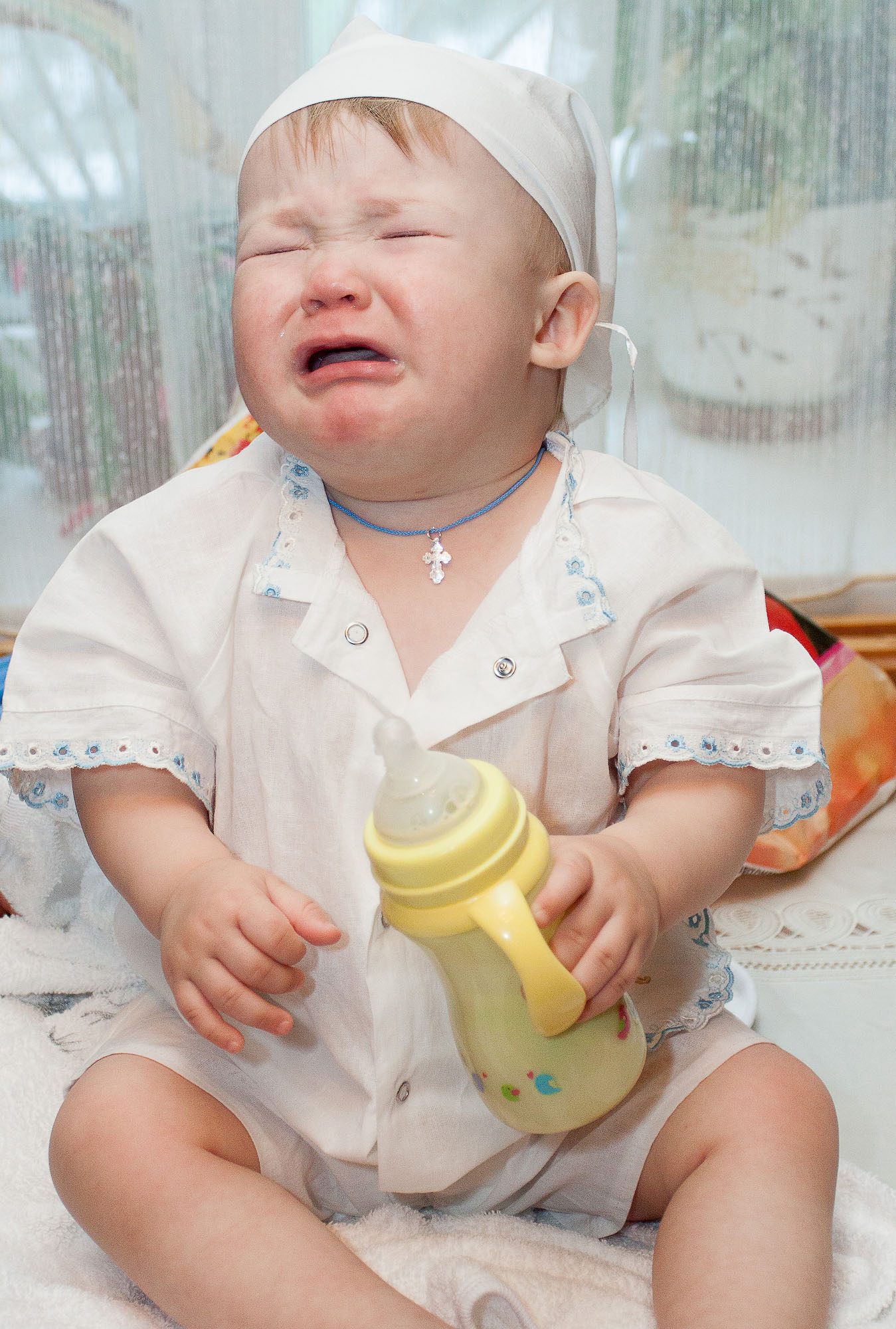 Мальчик в белой одежде для крещения с бутылочкой в руке плачек.