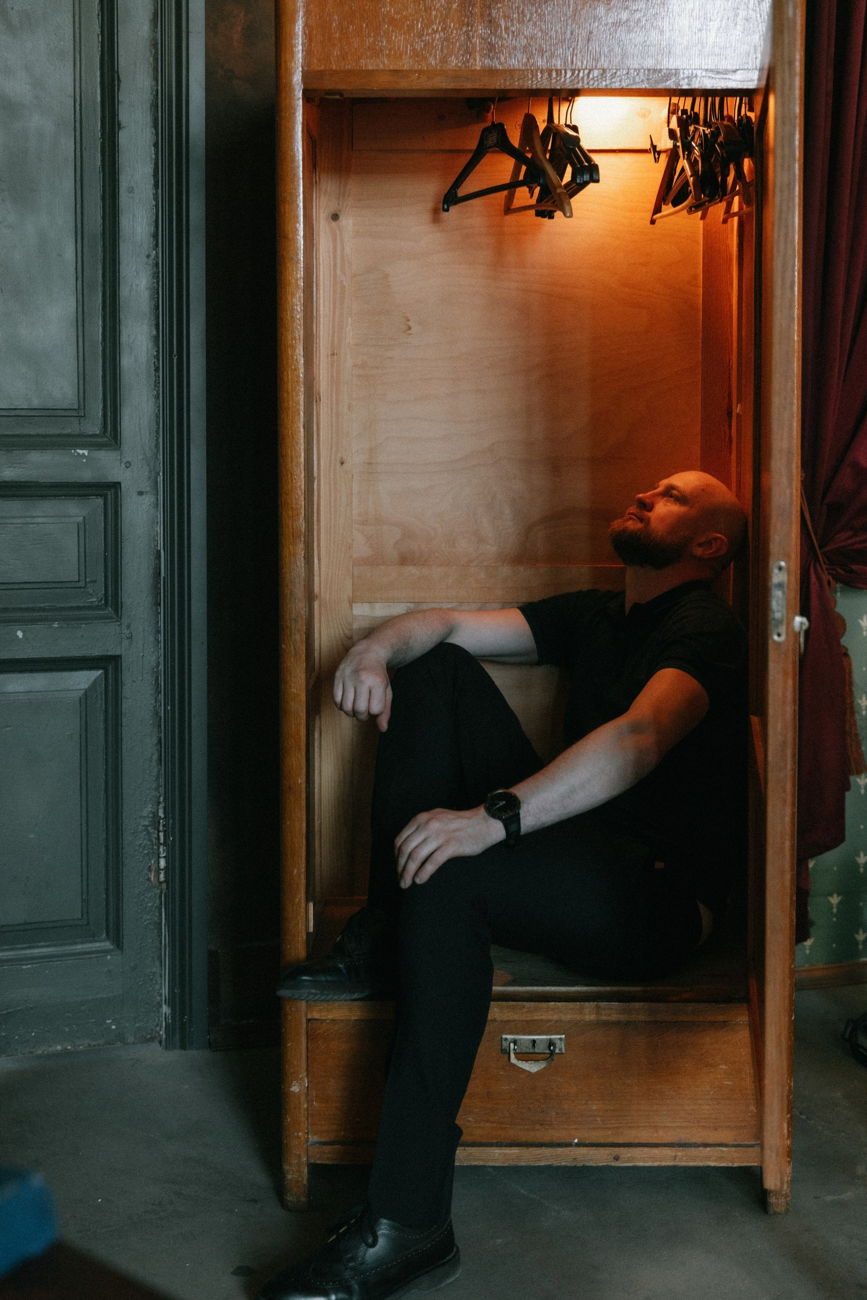 Мужчина задумчиво сидит в шкафу, необычный портрет в интерьере, фотосессия в Санкт-Петербурге.