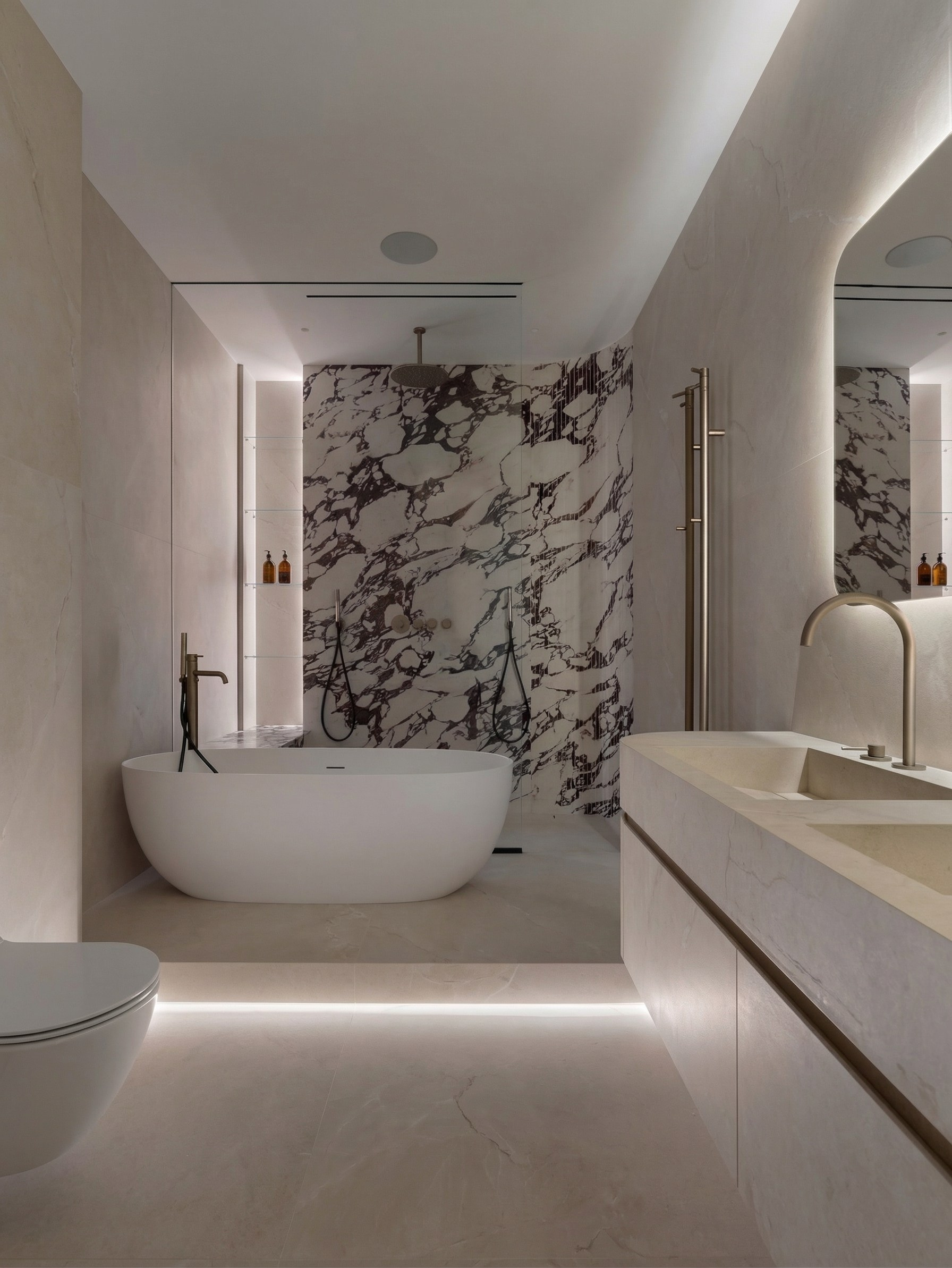 Дизайн ванной комнаты в современном премиальном стиле, проект квартиры 85 м² от Валерии Котович: акцентное каменное панно, парящая подсветка пола и латунная сантехника.