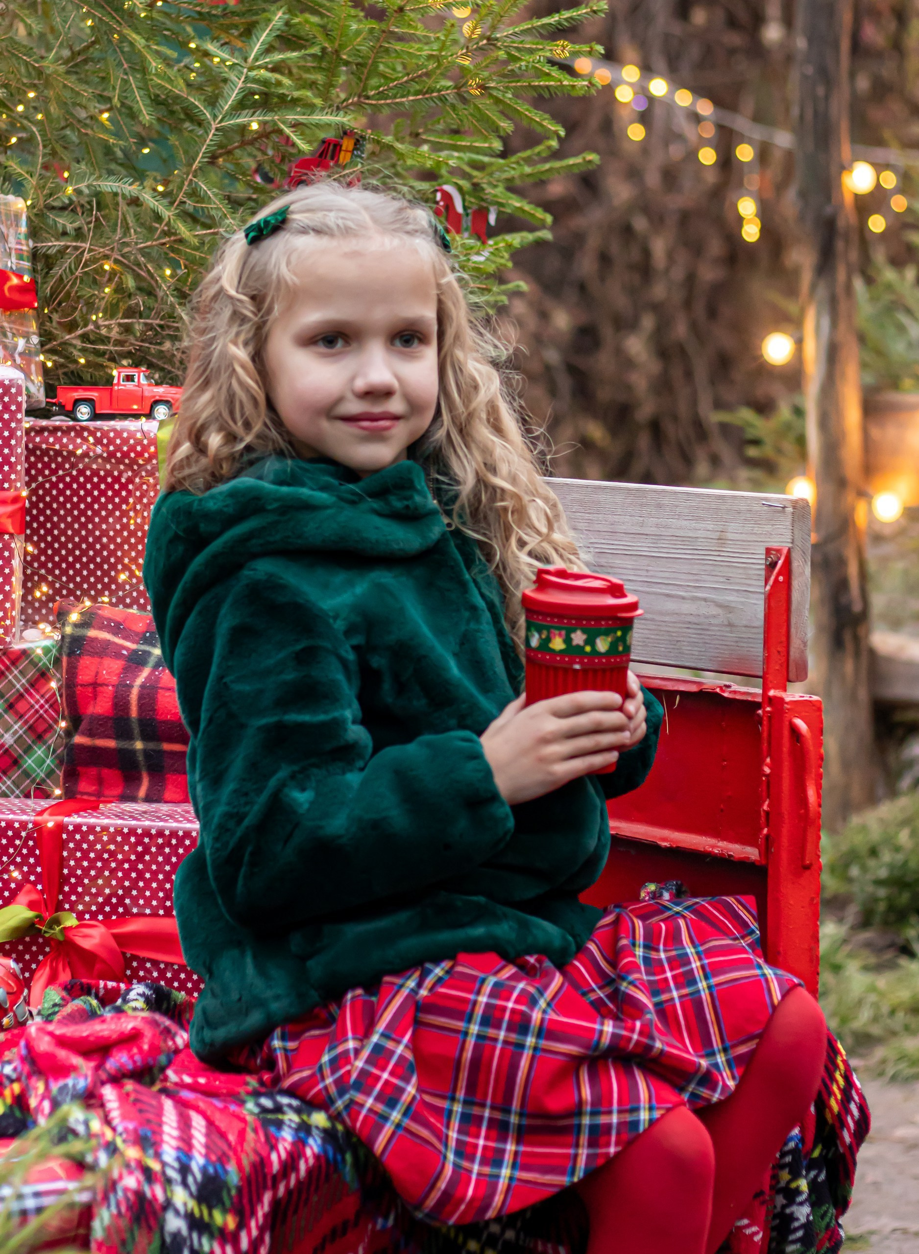 Новогодний портрет девочки в зелёной шубке и клетчатой юбке на фоне огоньков, фотограф Карасёва Елена