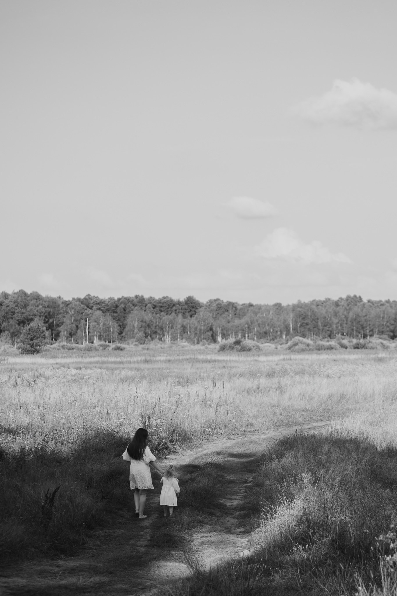 На чёрно-белом фото мама с дочкой идут по лесной тропинке. Вокруг — поле, деревья, спокойствие и умиротворение.