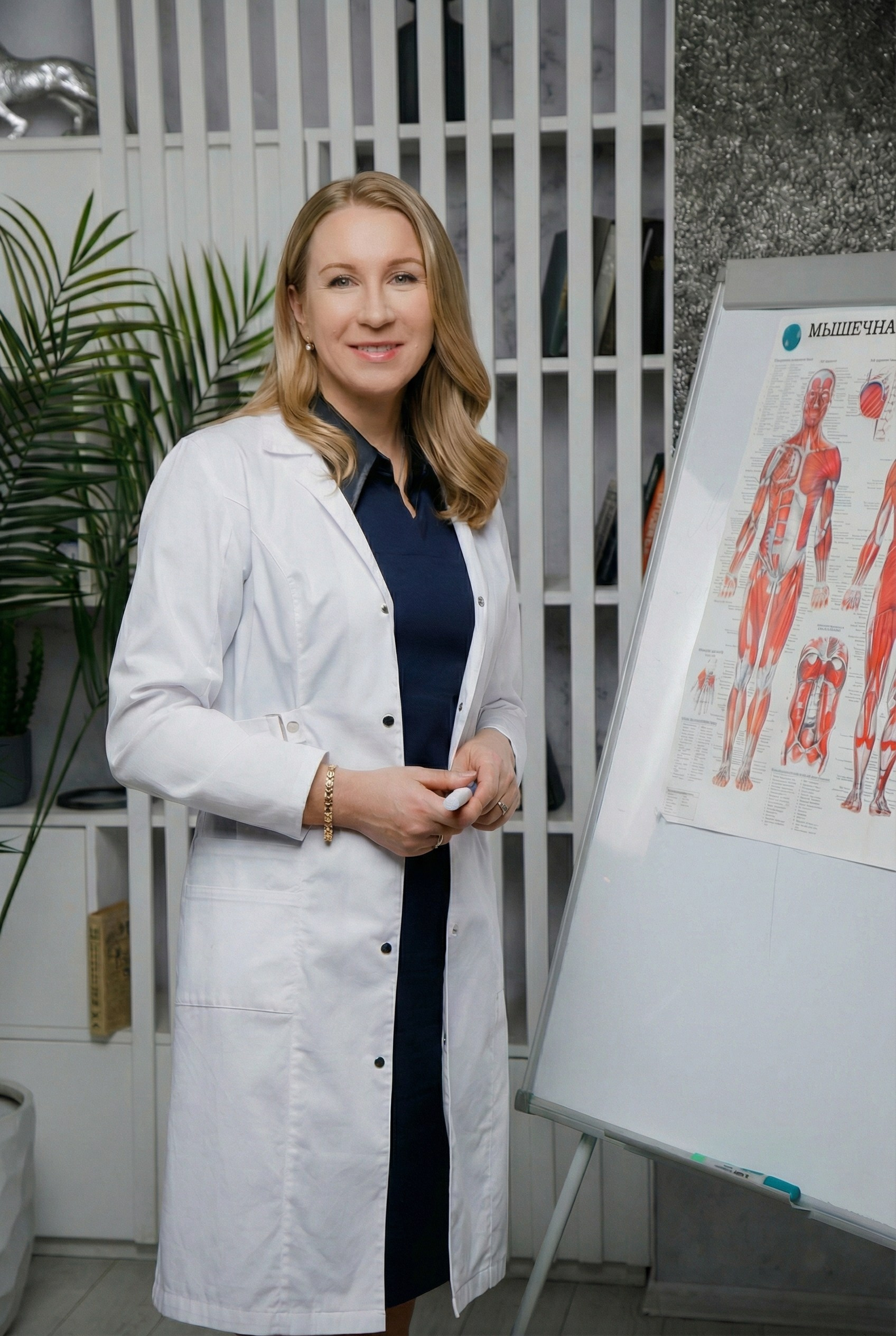 Женщина в халате врача стоит у доски с изображение внутренних частей организма