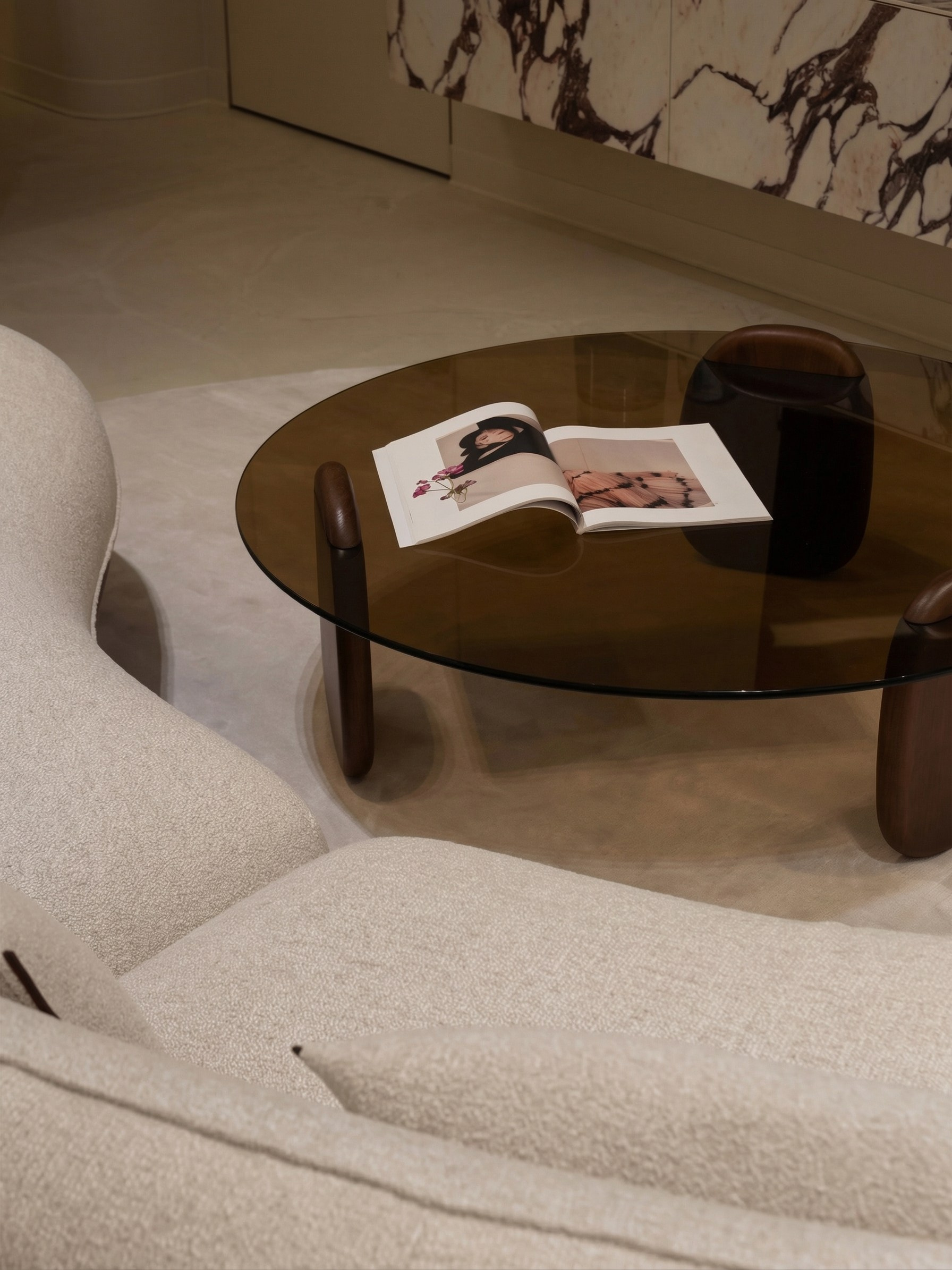 Деталь интерьера гостиной от Валерии Котович: стеклянный журнальный стол, диван букле и каменные фасады в современном премиальном стиле.