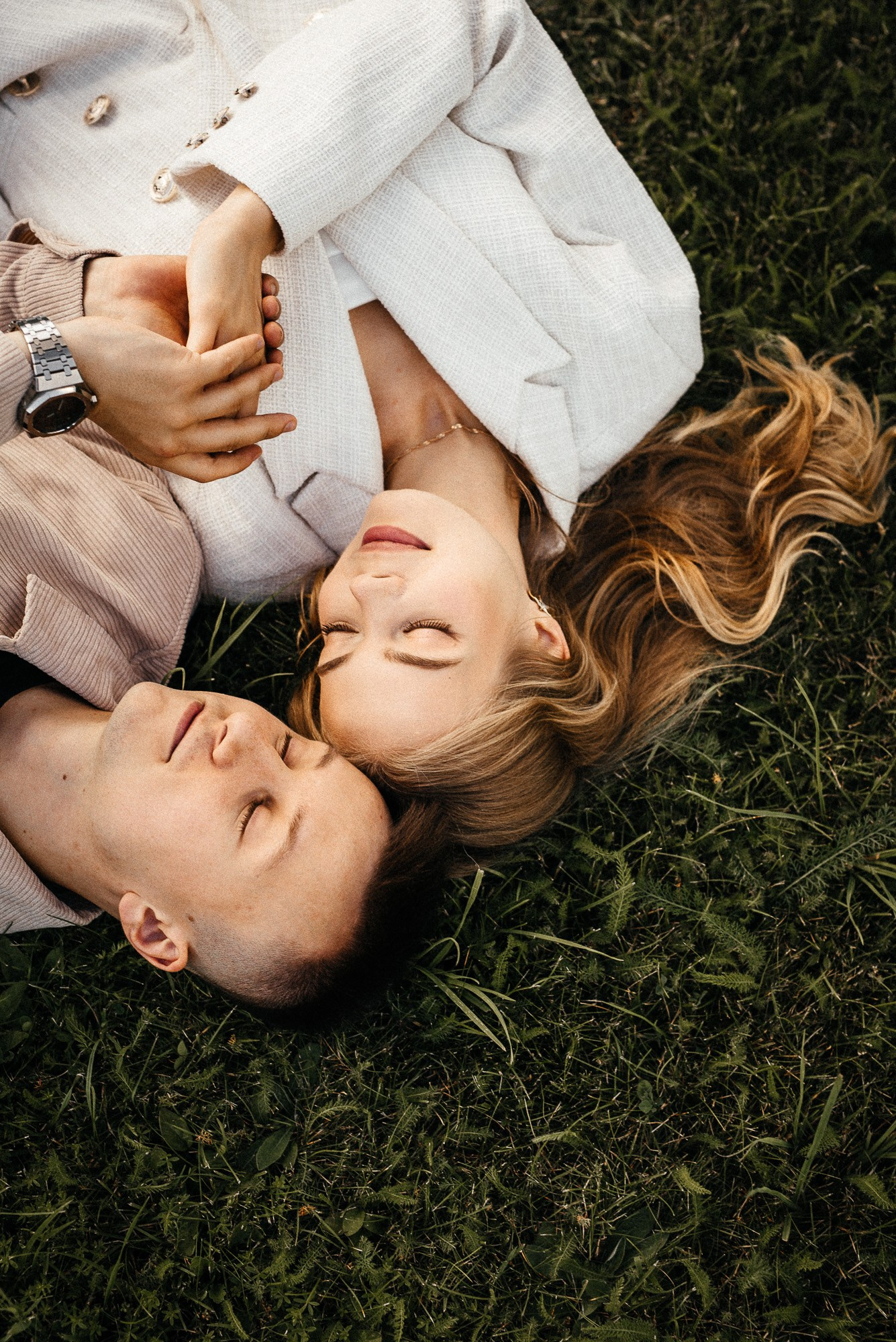 Молодожены лежат на траве, взявшись за руки, в парке Ораниенбаума