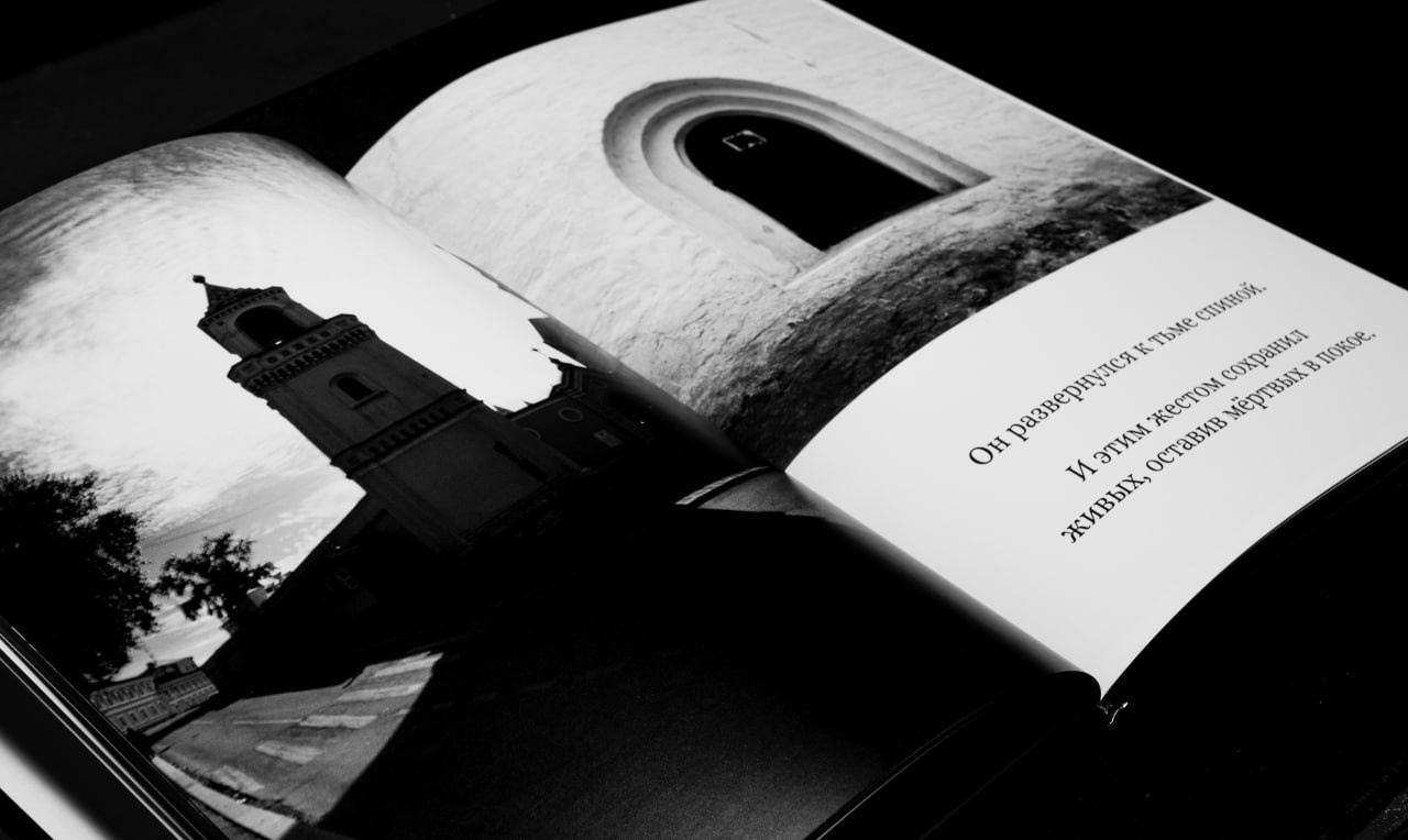 На изображении представлена открытая книга "Манифест теней". Страницы книги содержат текст, который начинается с фразы "Он разверзнется к тьме спиной". На левой странице видна фотография, на которой изображена церковь с колокольней на фоне неба. Фотография выполнена в черно-белых тонах.