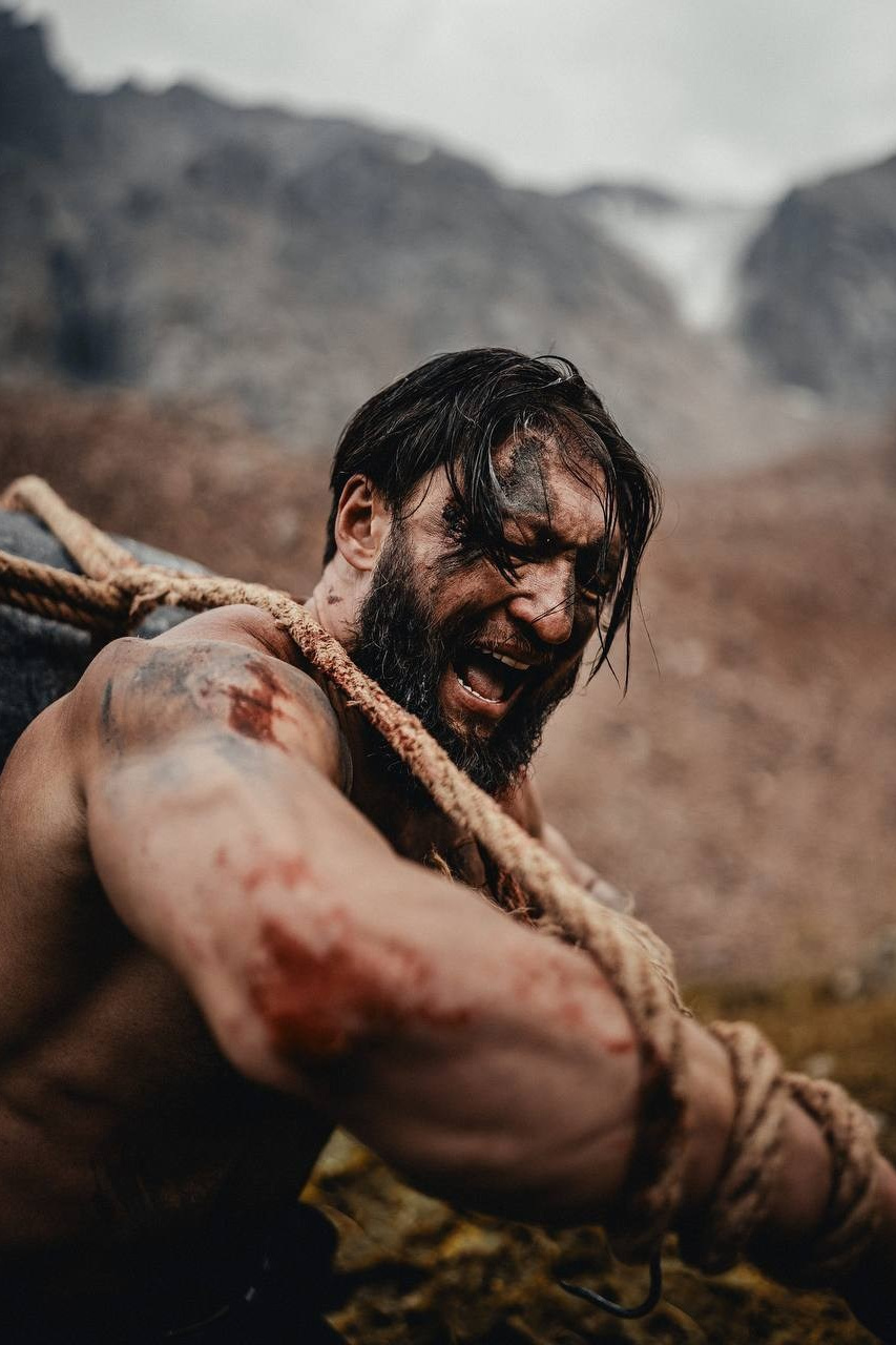 Мужчина с длинной бородой и грязным лицом тянет за собой большой камень в горах