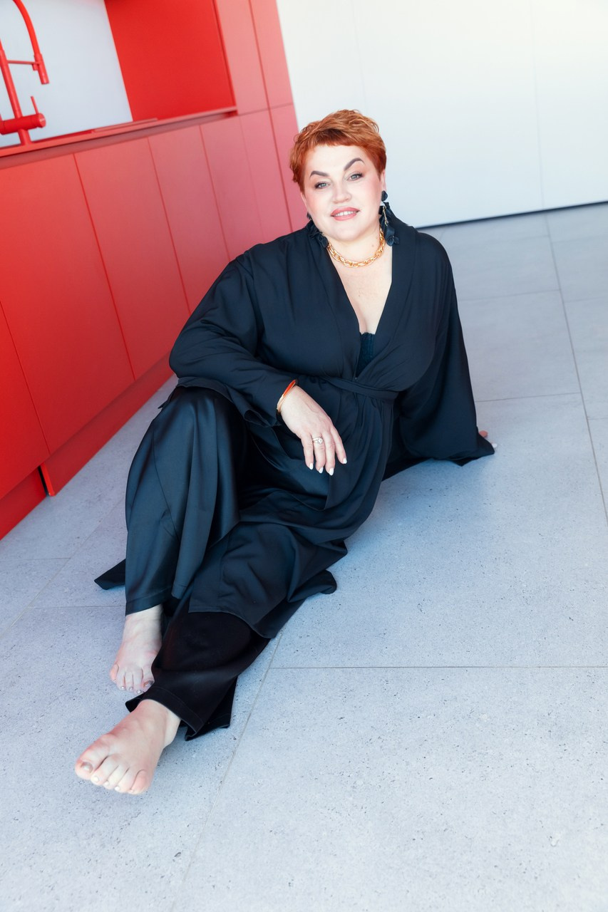 красивая женщина плюс сайз позирует на полу в черном кимоно в студии с красной мебелью