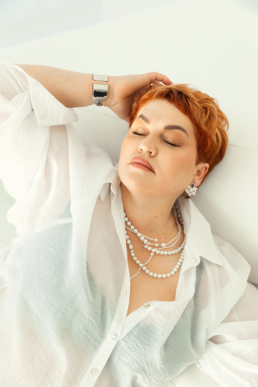 девушка с короткой стрижкой позирует лежа в легкой белой блузе, лежа