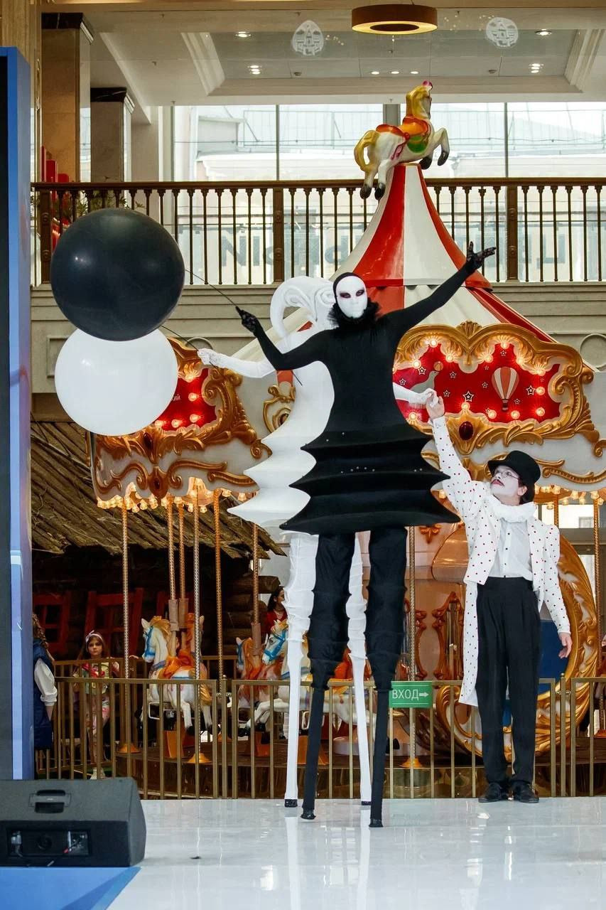 Ходулисты в белом и чёрном костюме выступают на подиуме.