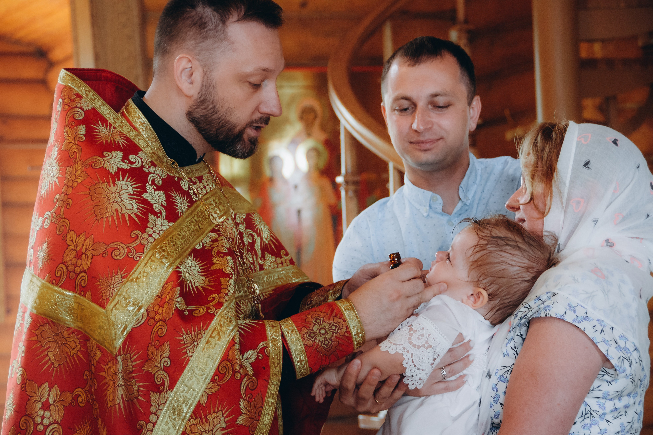 Крестная мать примеряет крестильную рубашку двухмесячной девочке, держа её на руках, после совершения таинства Крещения, 