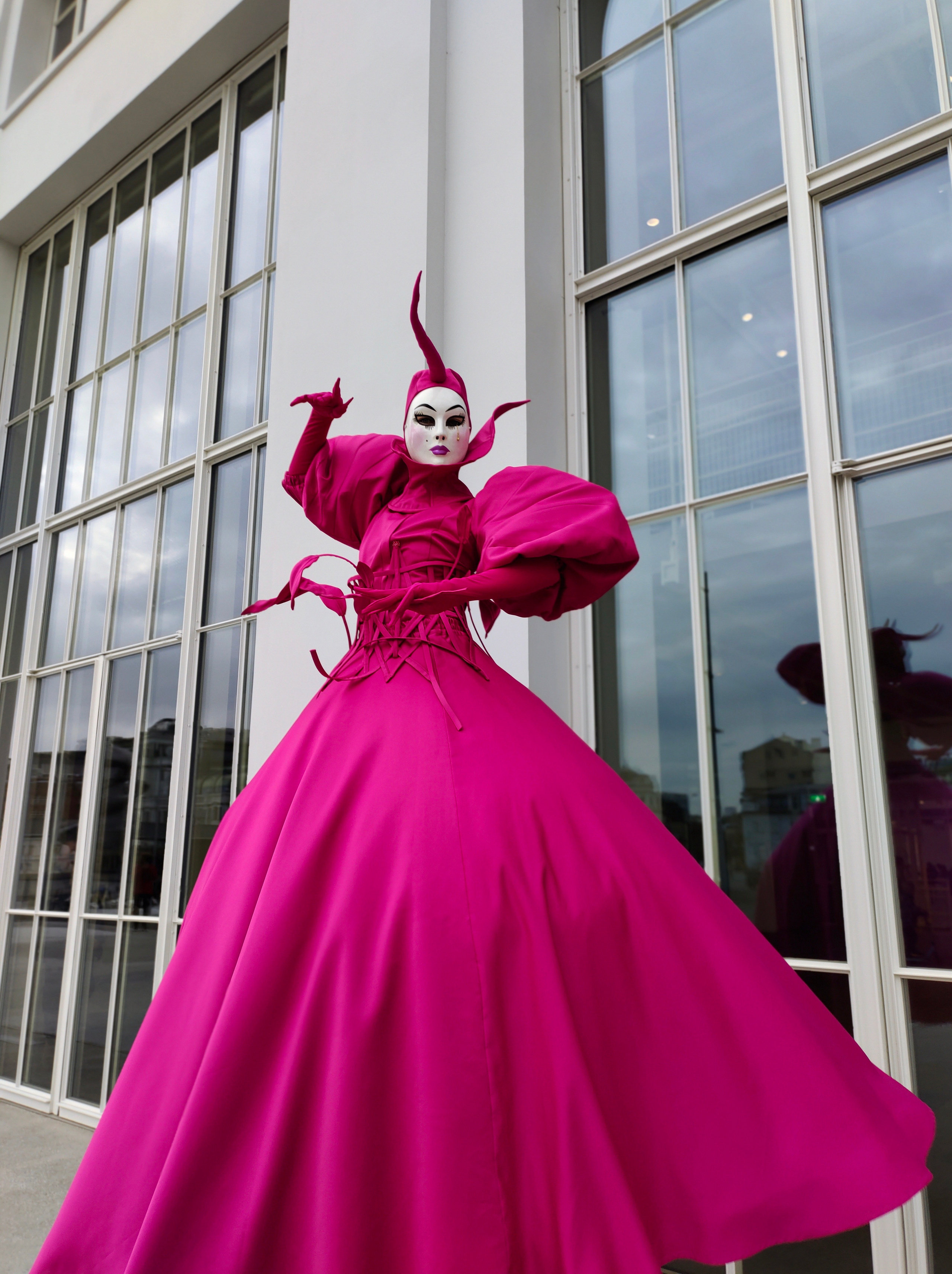 Танцующий ходулист в шикарном платье цвета Фуксии у ресторана на раусе вечеринке.