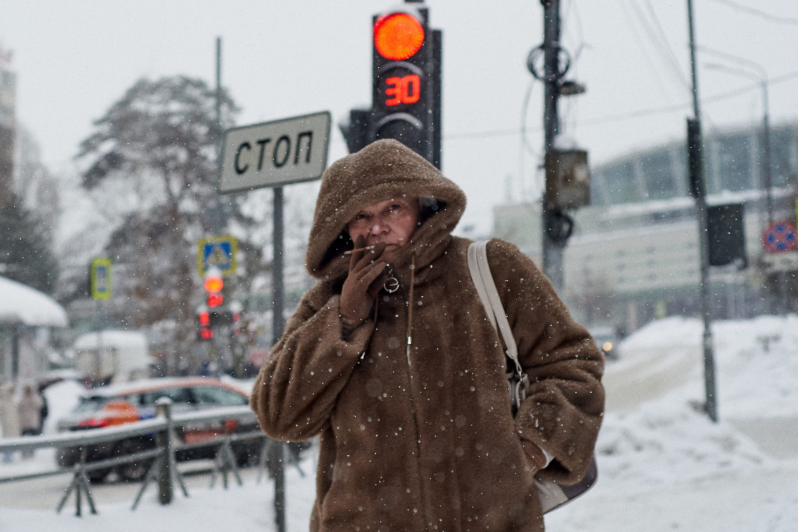 Woman smoking during snowfall. Young woman smoking a cigarette while standing on a snowy street in Moscow.